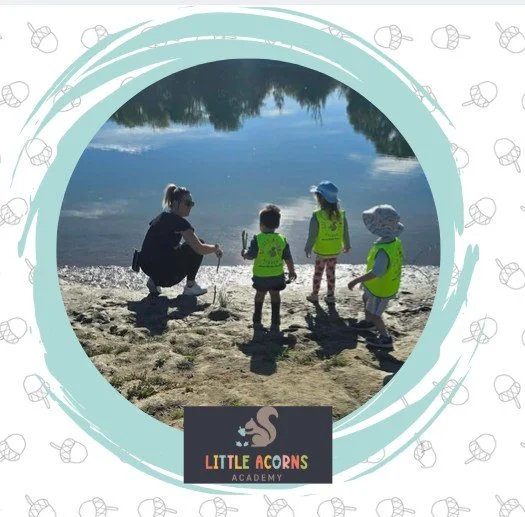 Four children at the lakeshore, wearing yellow vests, with a dog and water reflections in the background.