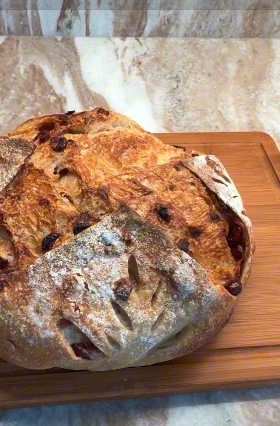 Cranberry orange olive oil sourdough loaf with a crusty exterior on a wooden cutting board, set against a stone backsplash.