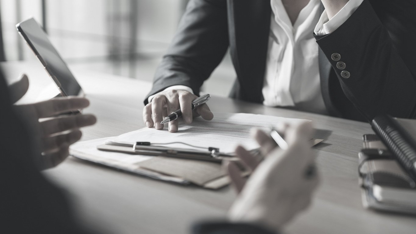Business professionals discussing documents and using smartphones at a table in an office.