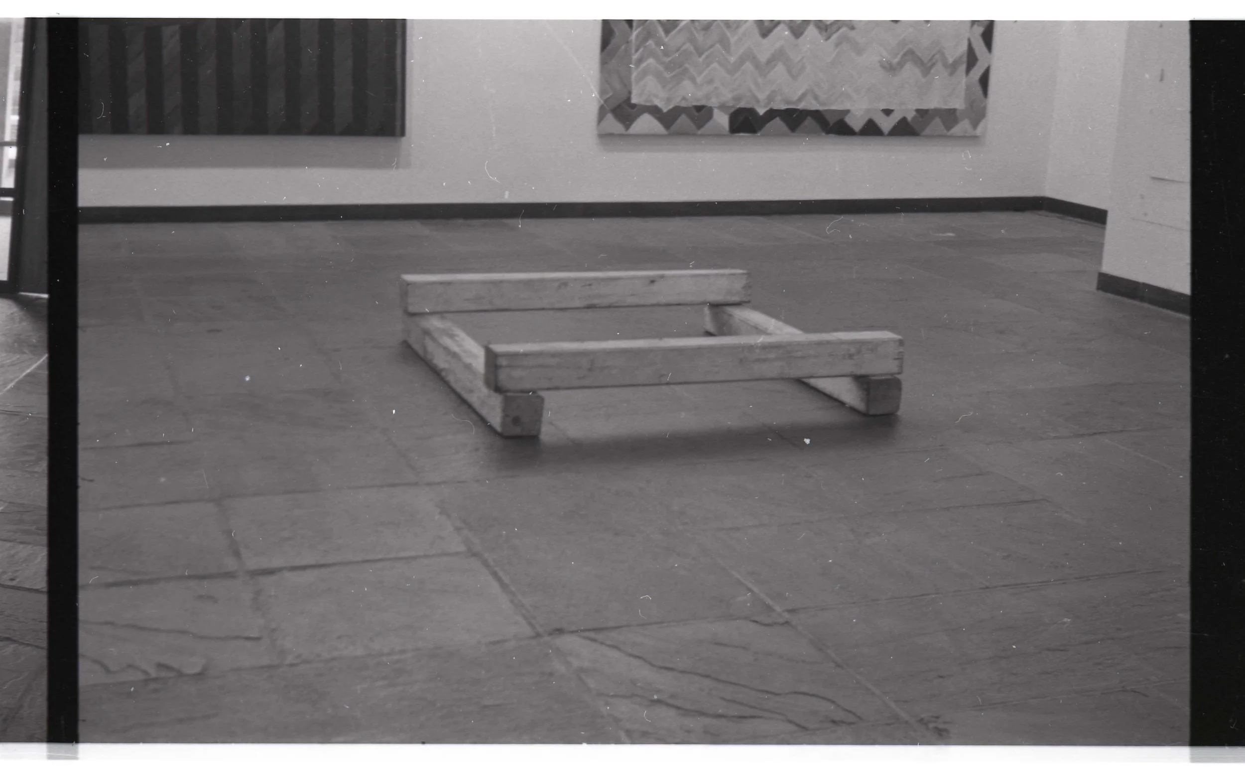 An empty wooden pallet on a tiled floor in a room with paintings or rugs hanging on the wall.