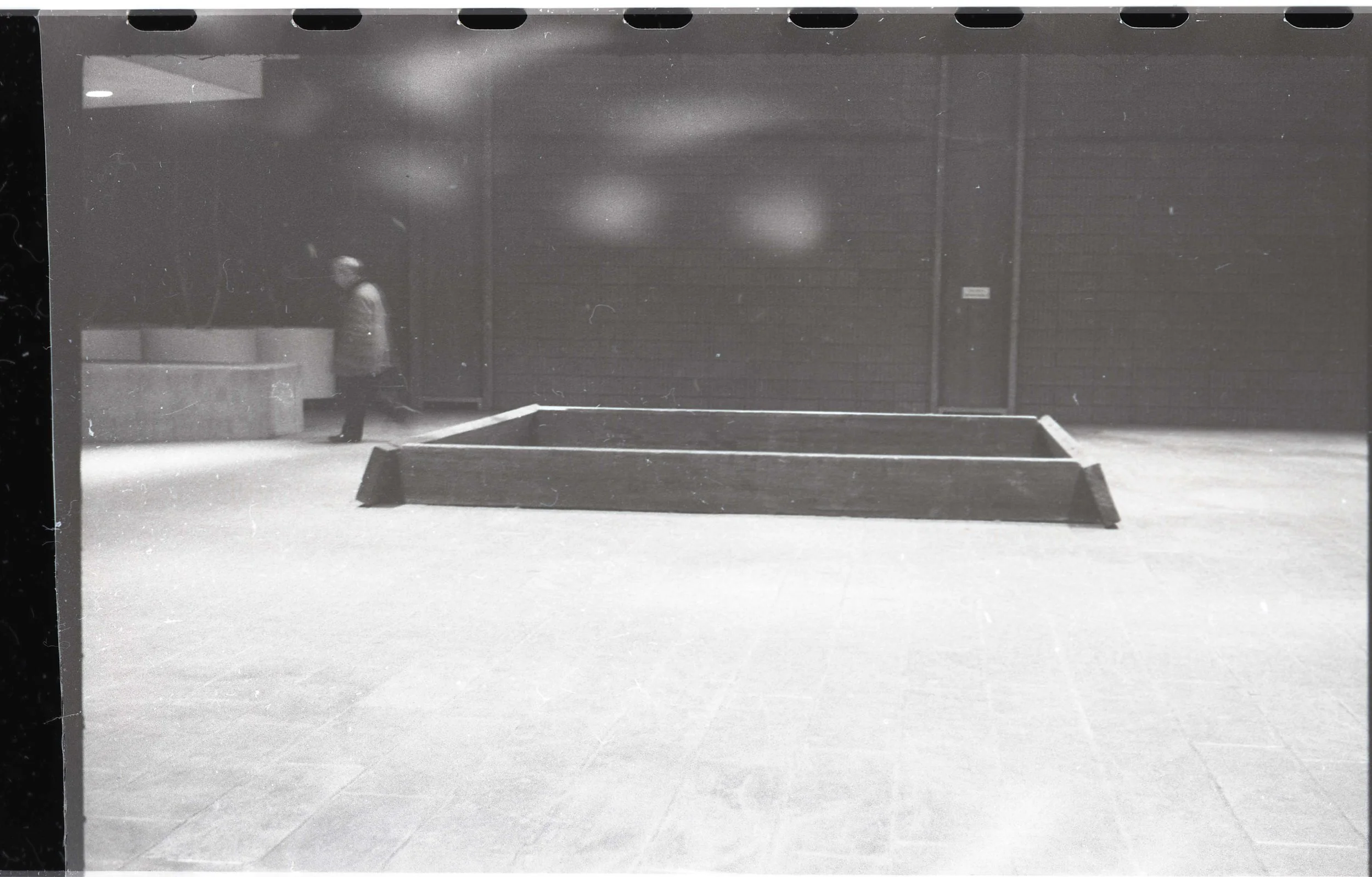 A person playing ping pong in an indoor room with a wooden barrier behind them and walls with a textured surface.