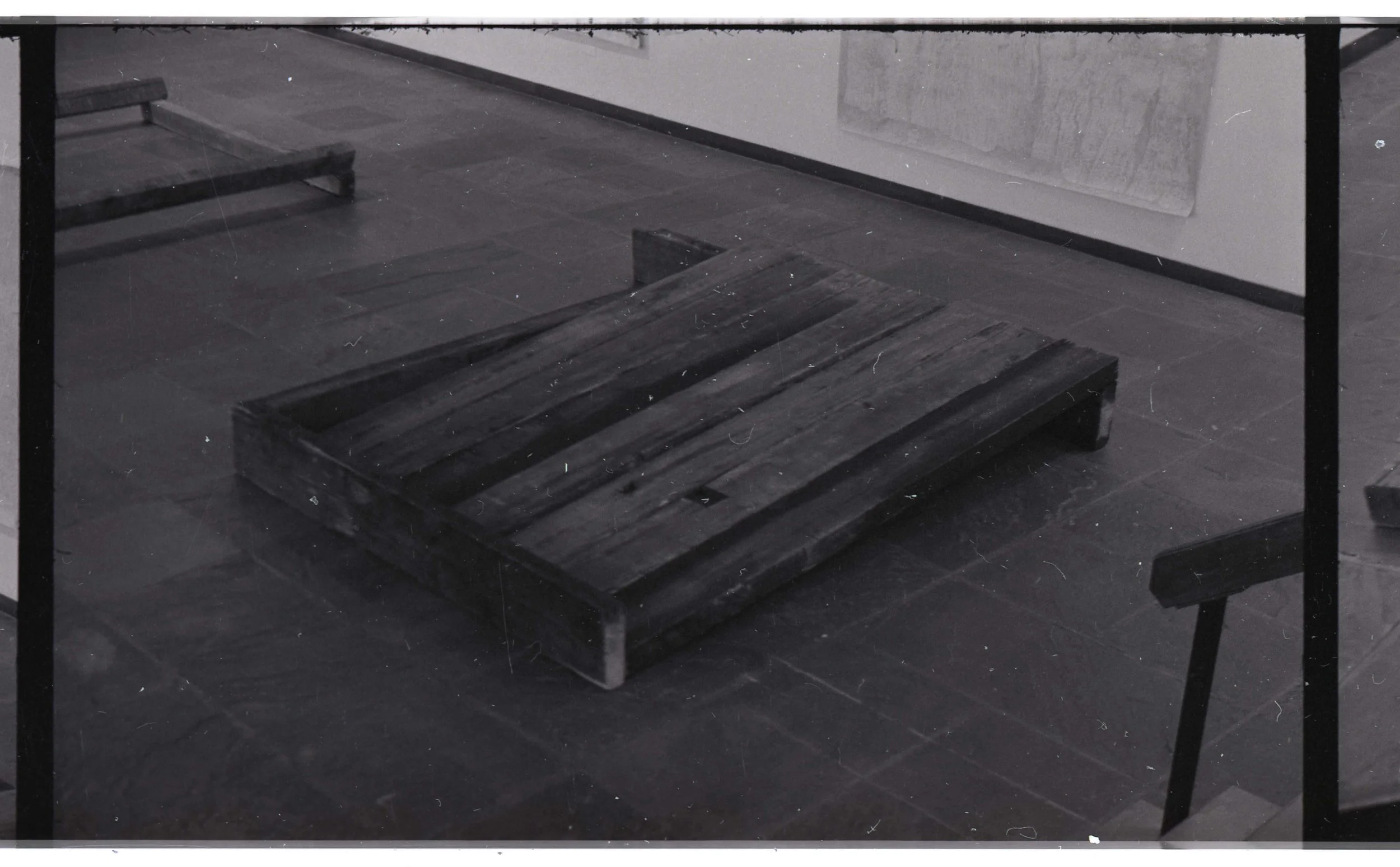 A wooden pallet table in a room with a dark floor and a white wall with a framed artwork or poster.