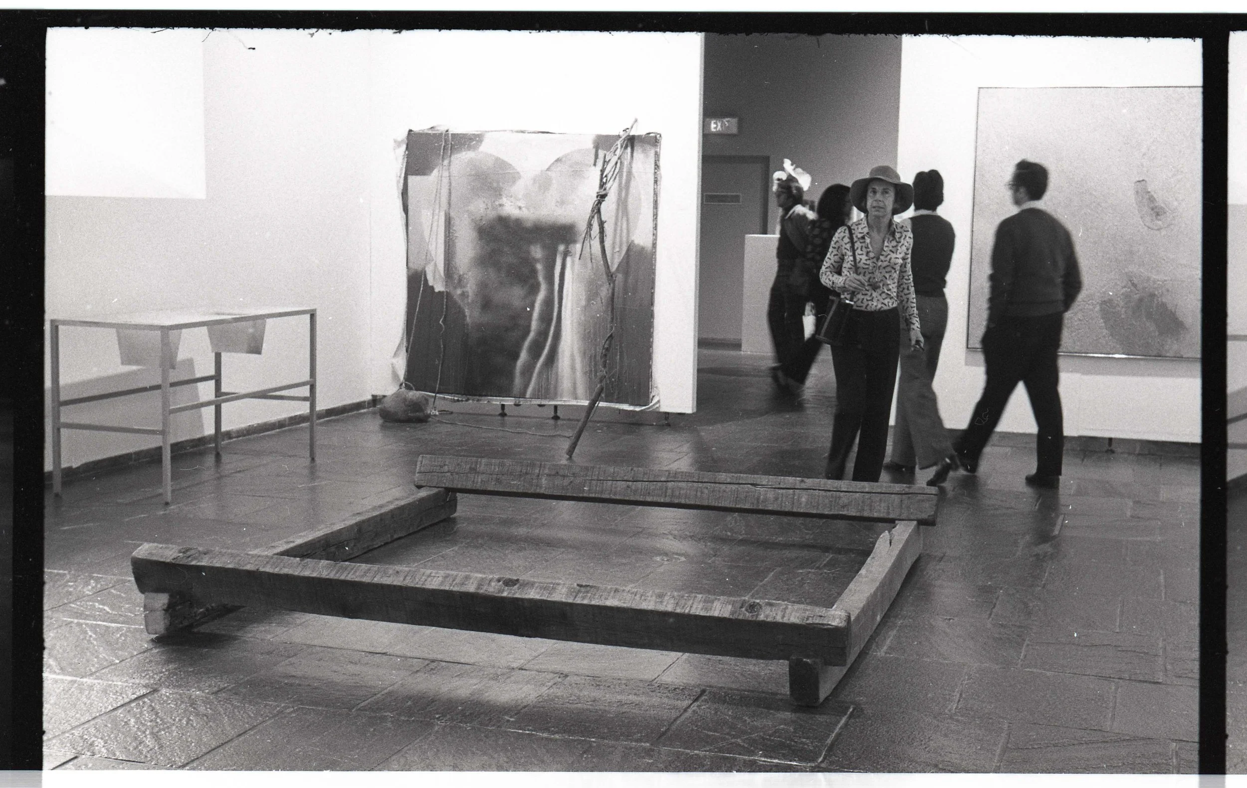 An art gallery with paintings on the walls and a group of people viewing the artwork.