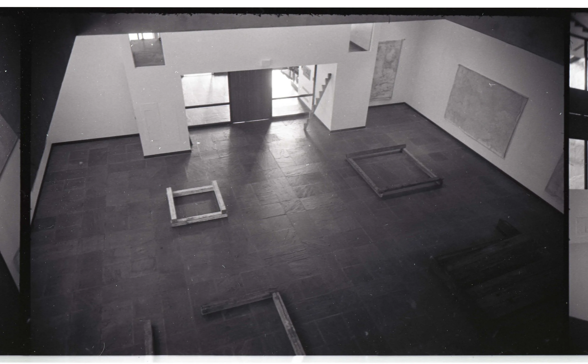 Empty room with dark flooring, white walls, and some frames or structures on the floor, and large windows or glass doors in the background.