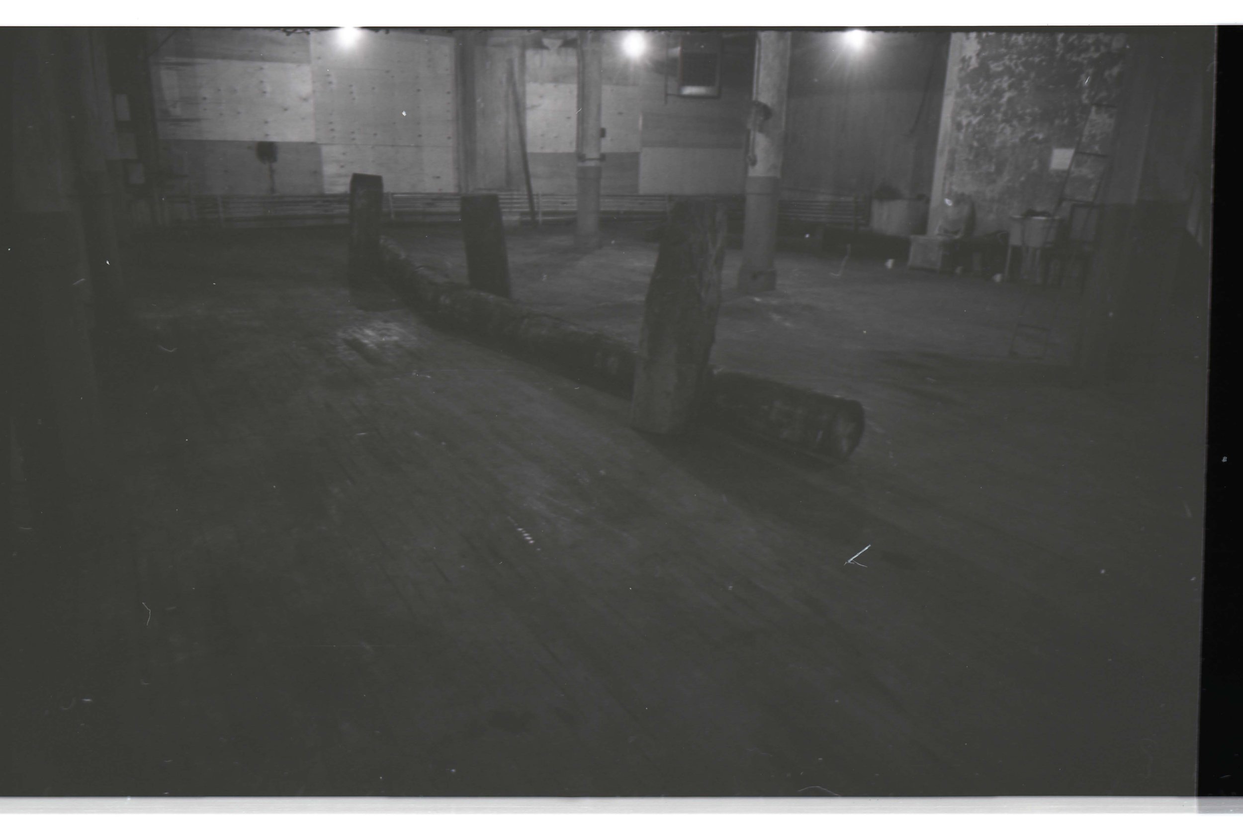 An empty wooden room with furniture including benches, chairs, and a work table. The room appears to be under construction or renovation.
