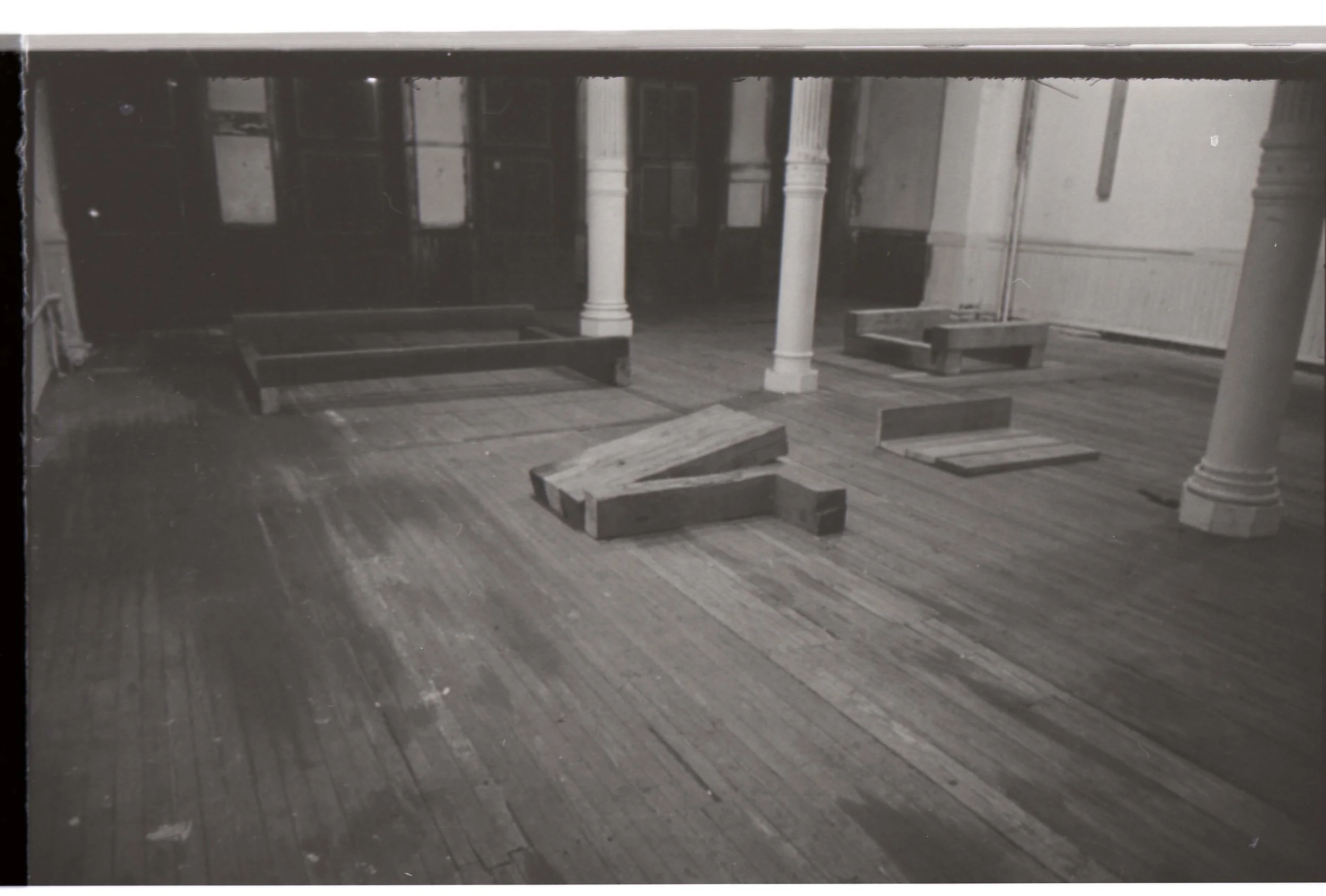An empty room with wooden floors, white columns, and furniture frames, possibly under renovation or construction.