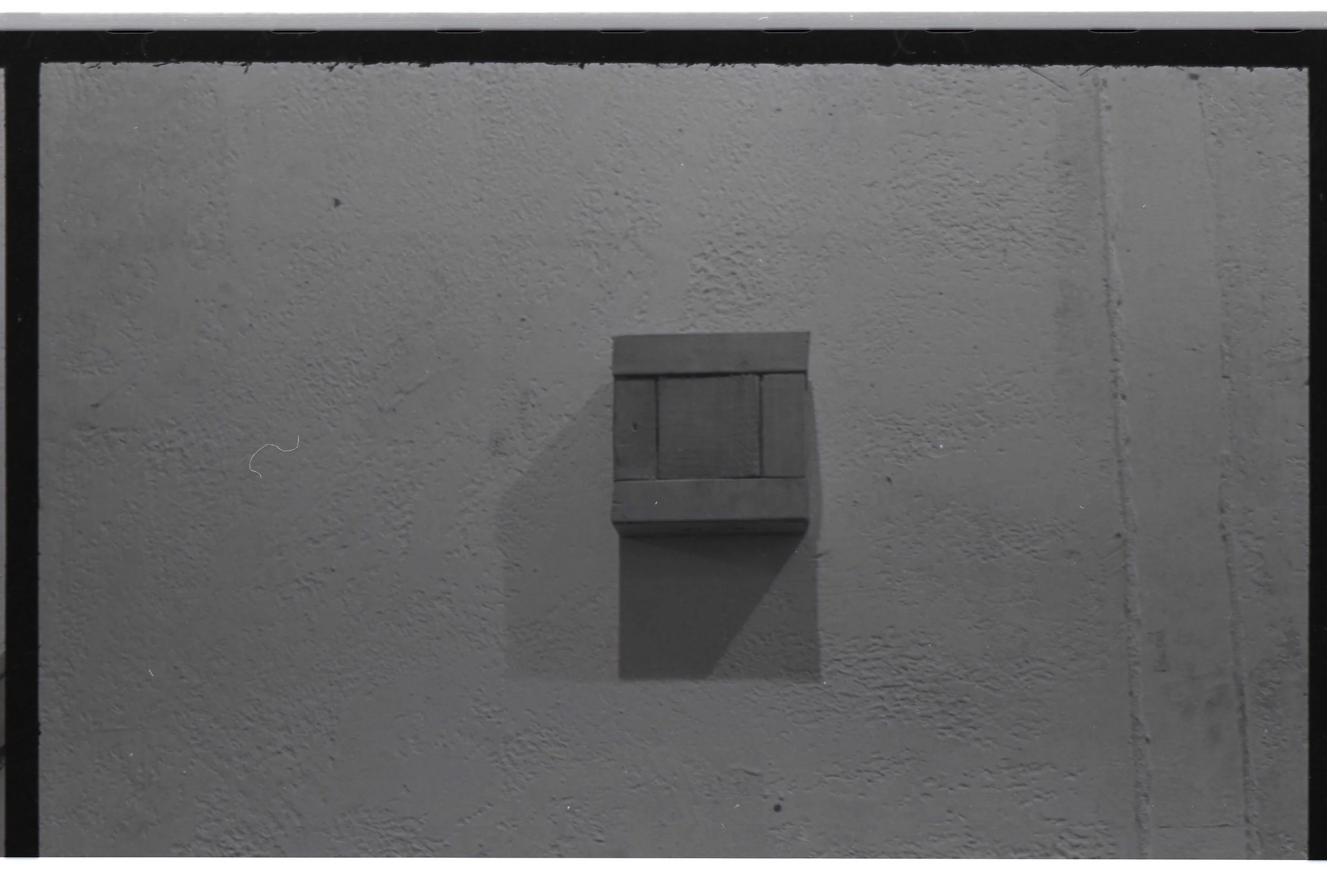 A small rectangular vent on a textured white wall, casting a shadow downward.