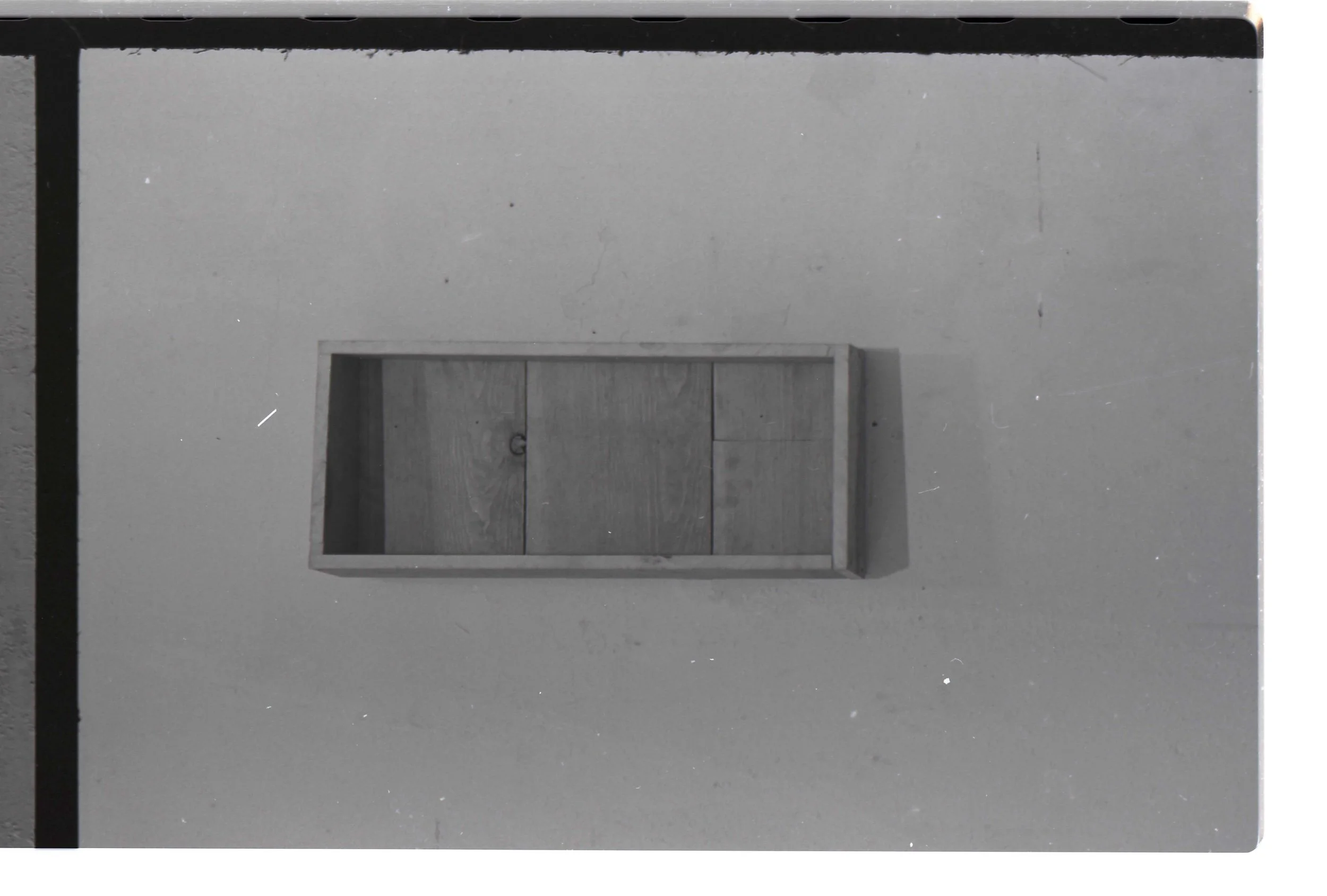 A black and white photograph of a staircase with a closed wooden door at the bottom. The staircase has a simple design with no visible handrails and appears to be in an indoor setting.