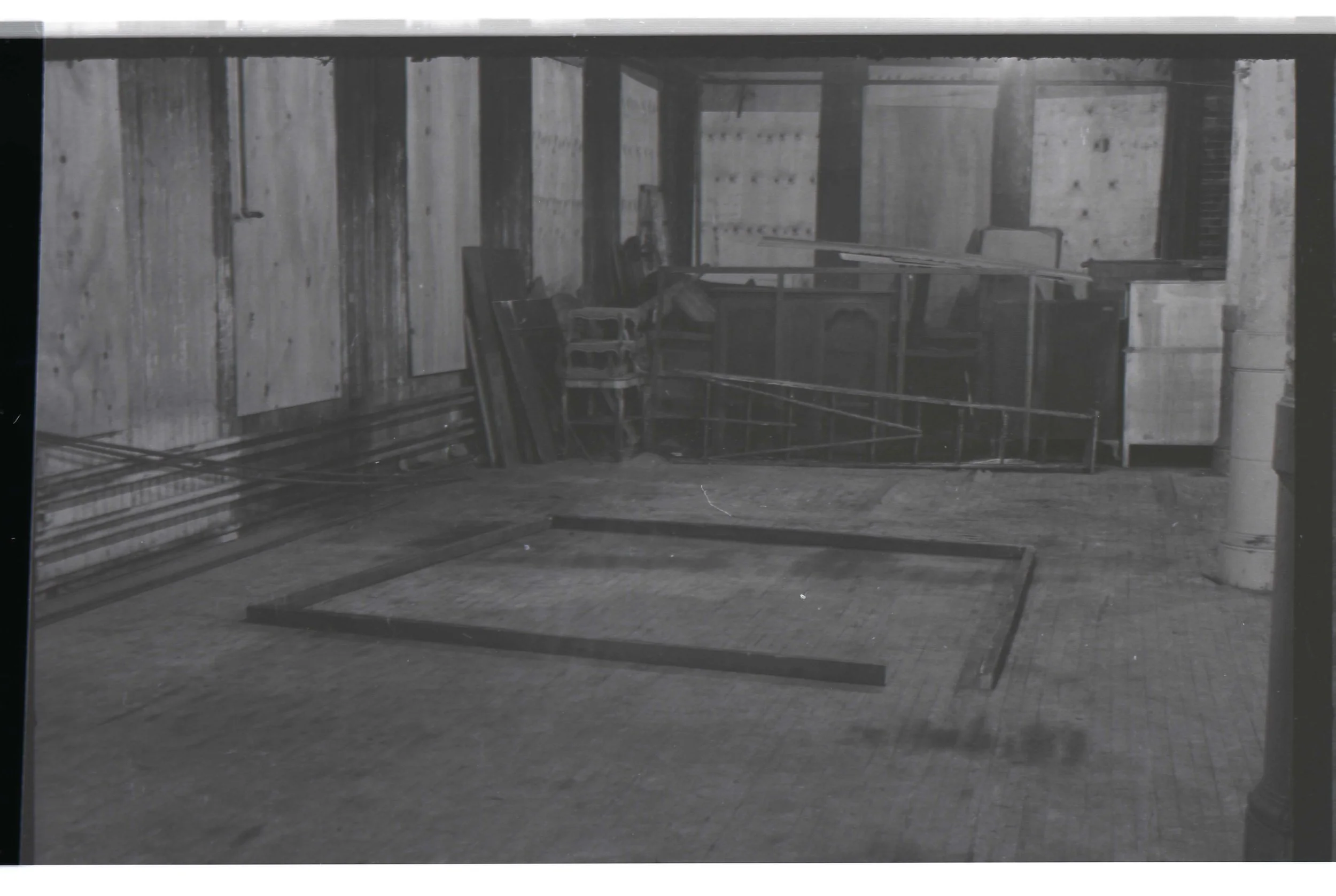 An unfinished room with wooden walls and ceiling, construction materials, chairs, and a metal frame on the floor.