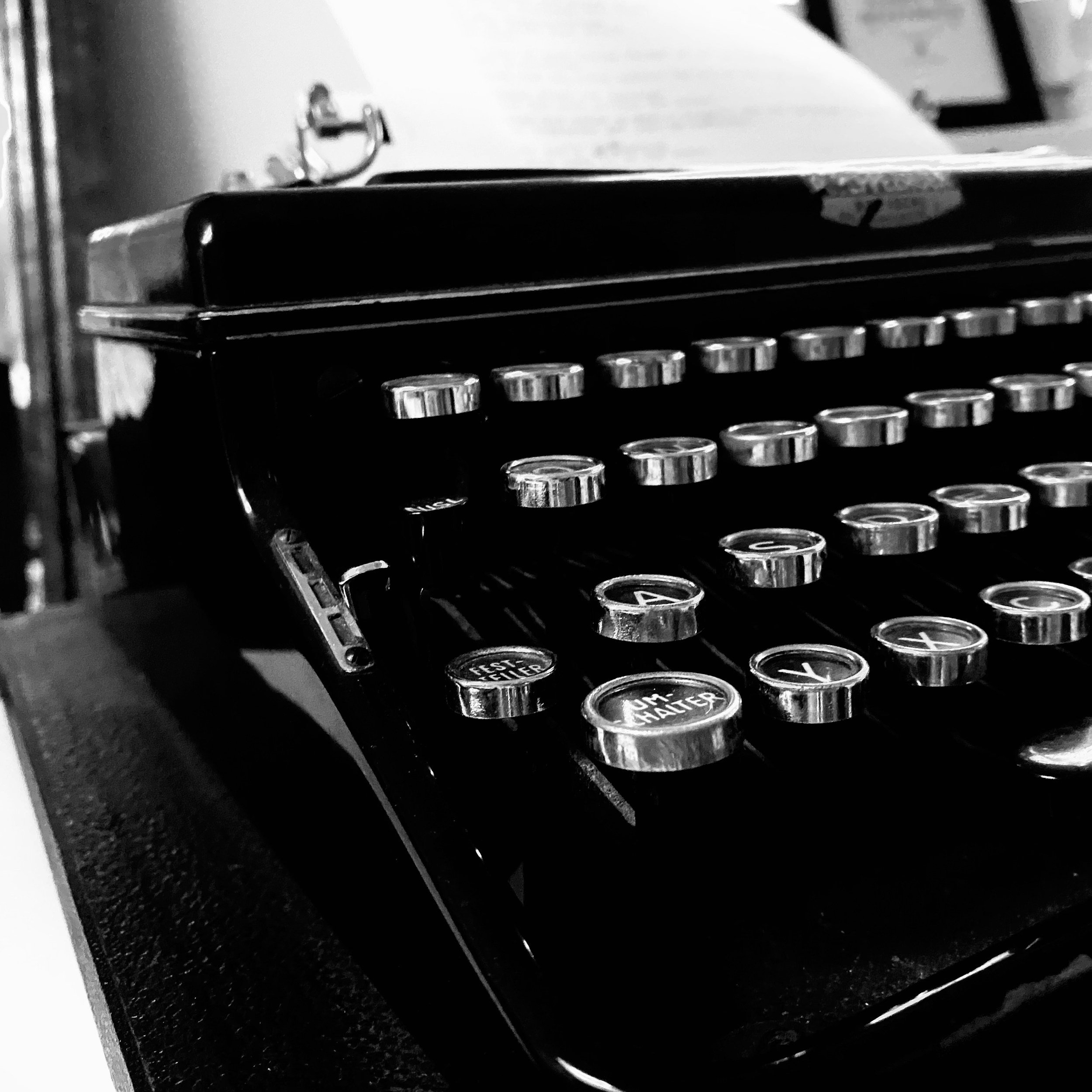 Close-up of a black vintage typewriter with round keys on a dark surface, black and white photography.