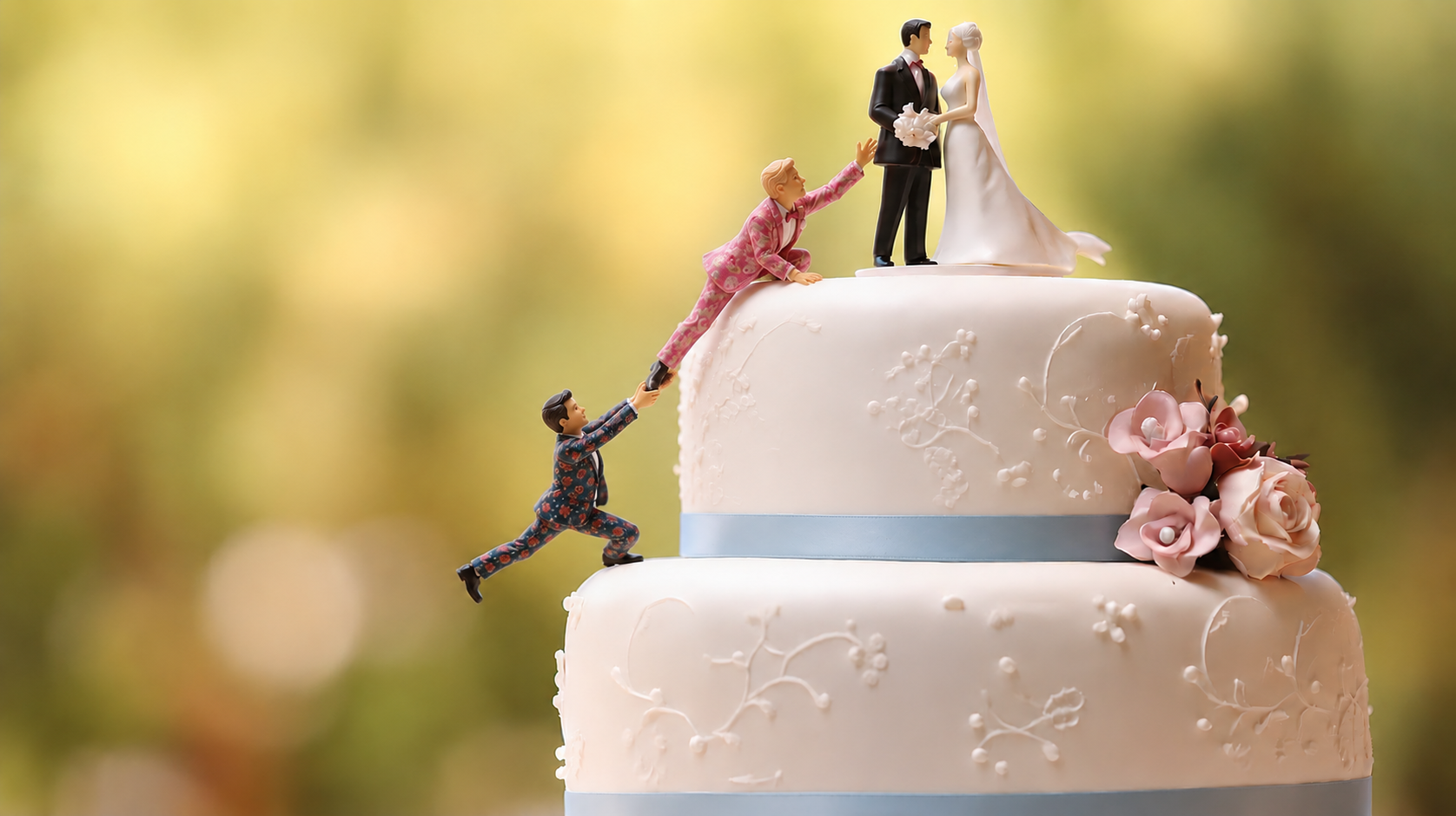 A wedding cake with figurines of a bride and groom on top, and a man in a floral suit helping a woman in a pink dress climb up the side of the cake.