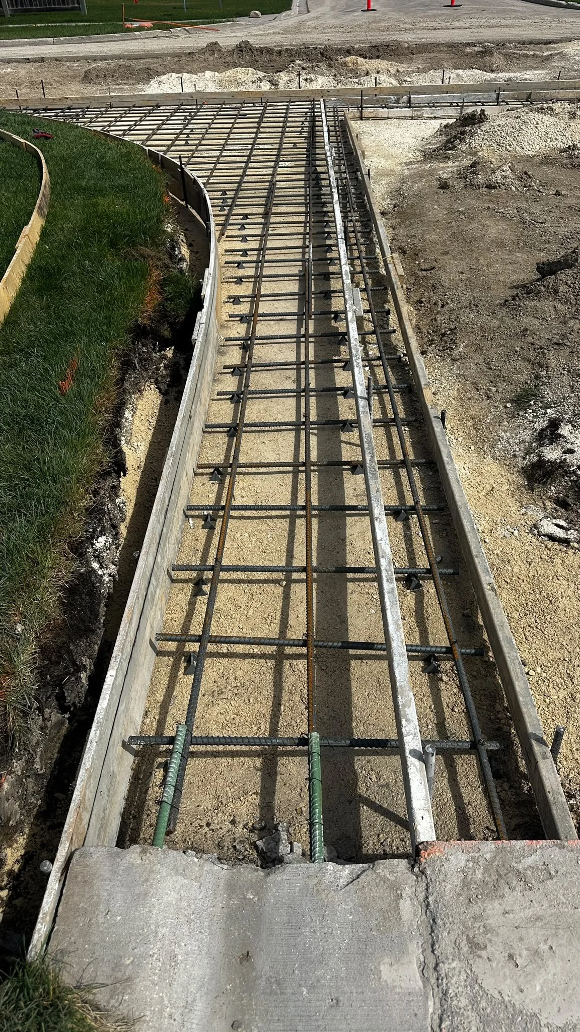 Construction site with metal rebar framework for a concrete sidewalk or pathway, gather line work by TSNA construction Group in Winnipeg Manitoba.