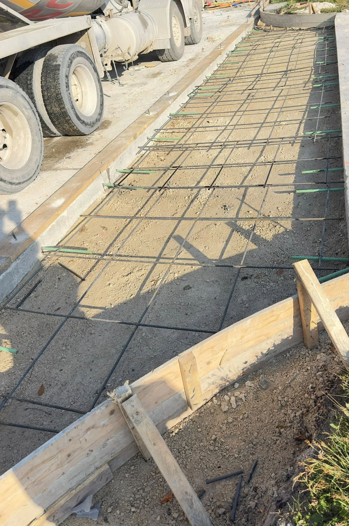 A construction site showing a concrete curb being formed, with wooden board forms and metal reinforcement bars in preparation for pouring concrete by TSNA construction Group in Winnipeg Manitoba.