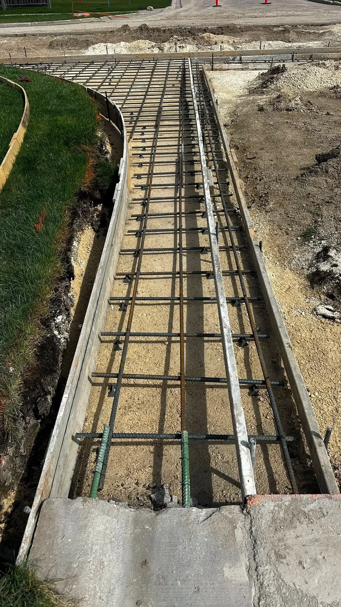 Concrete sidewalk with exposed rebar and formwork being prepared for pouring concrete