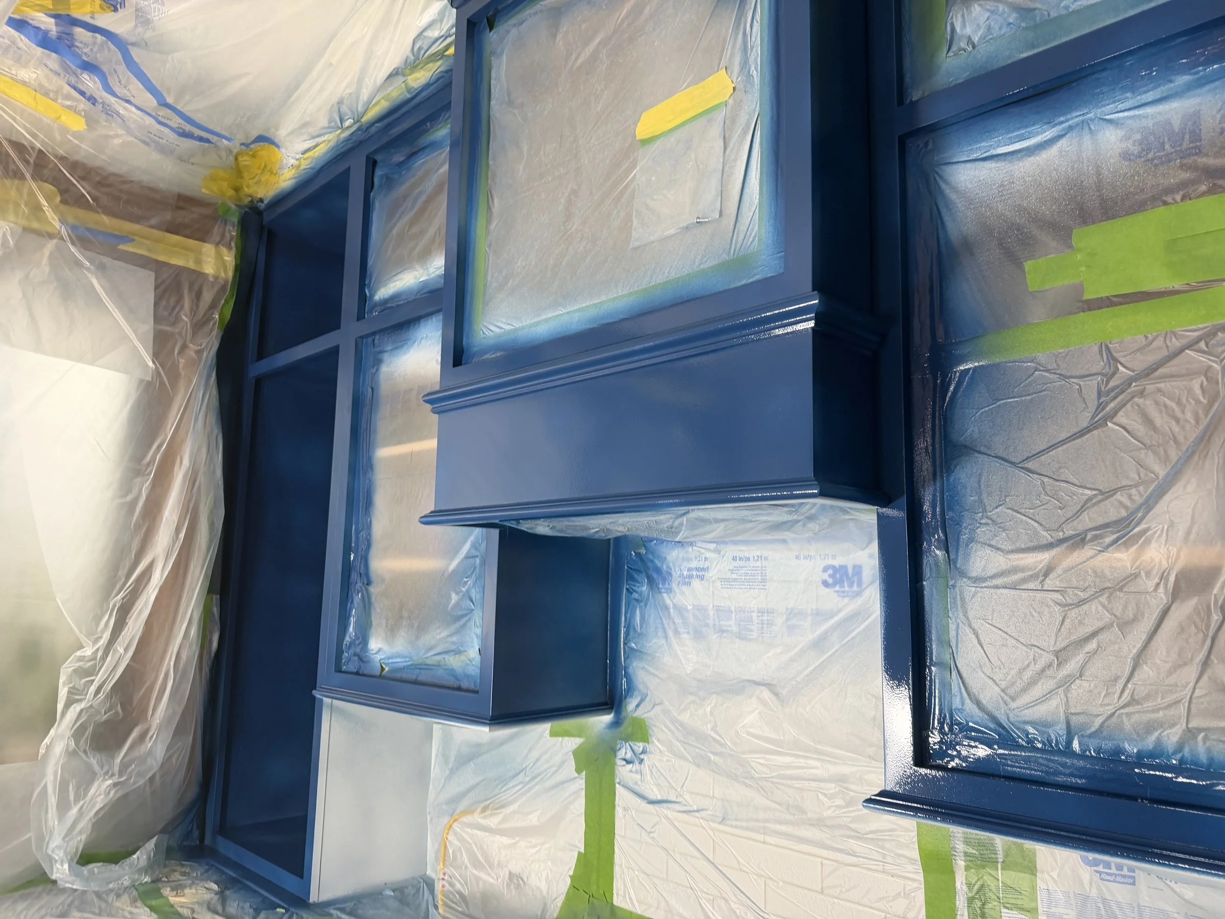 A blue cabinet or drawer unit covered in plastic and painter's tape, likely in preparation for painting or renovation.