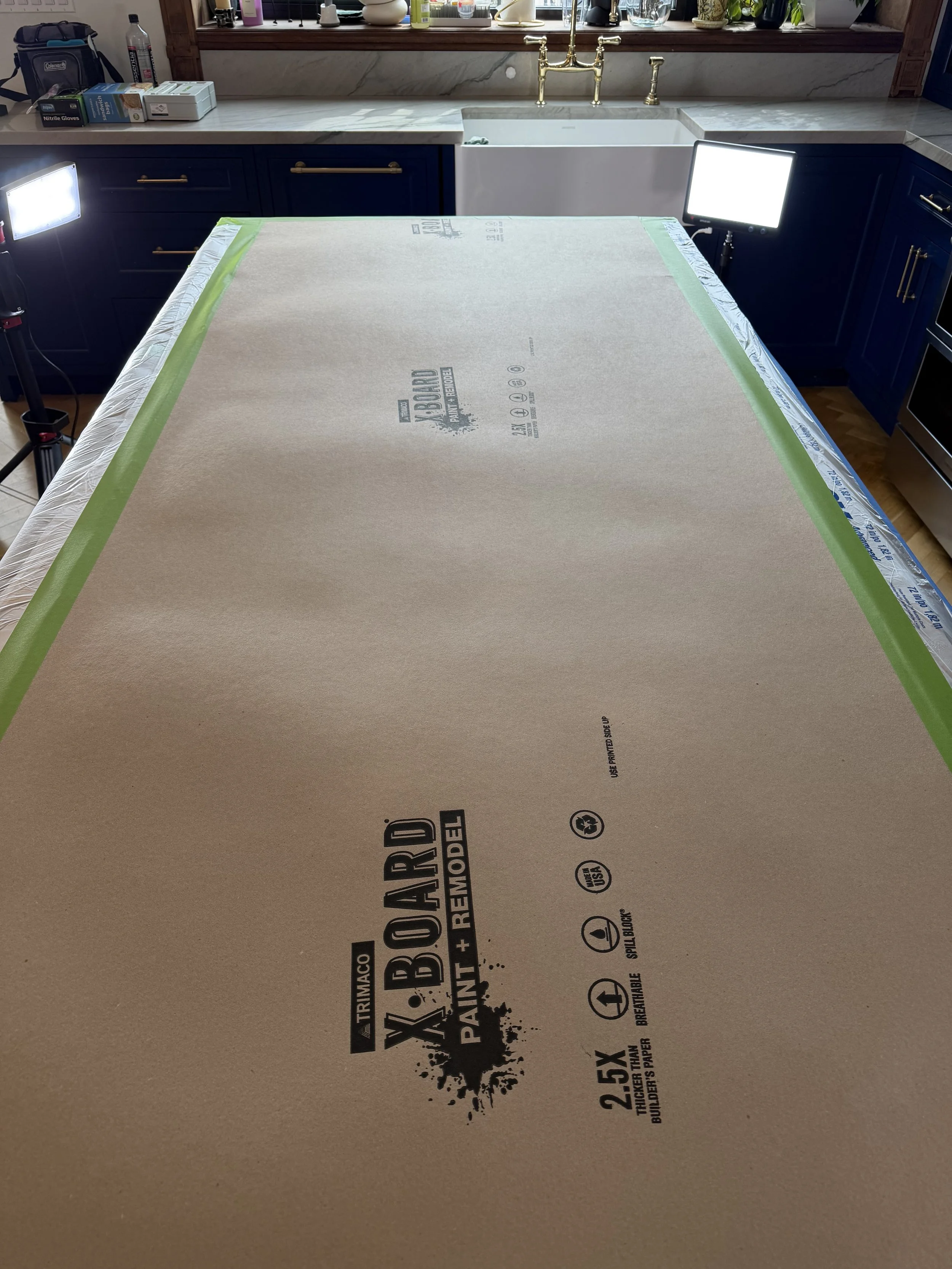 A large piece of brown packaging paper or cardboard with black printing and icons laid on a table, with a kitchen sink and countertop in the background.