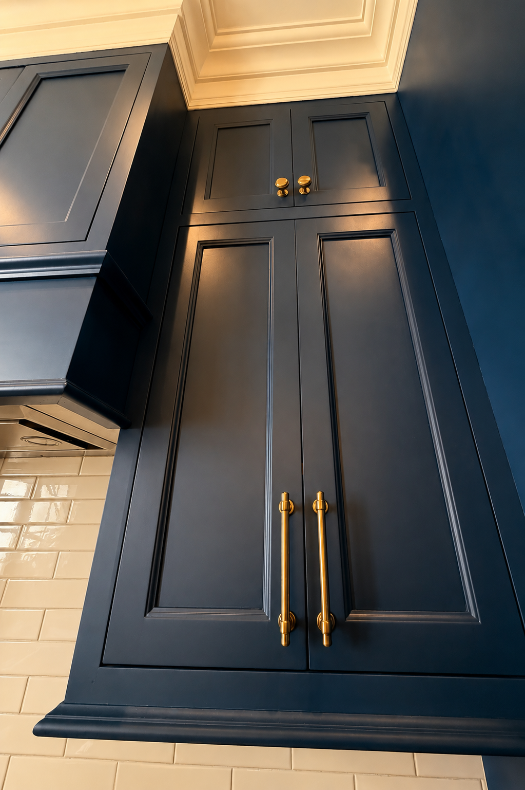 A dark blue kitchen cabinet with gold handles above a white subway tile backsplash.