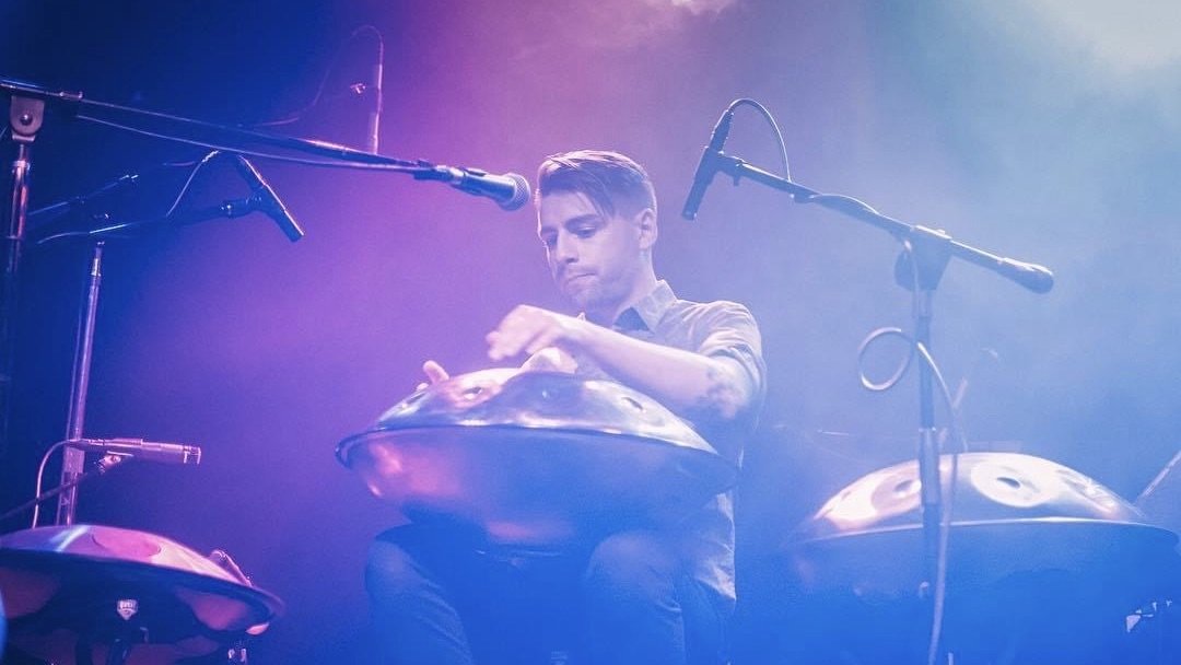 A man playing steel tongue drums on stage, surrounded by microphones with purple lighting.