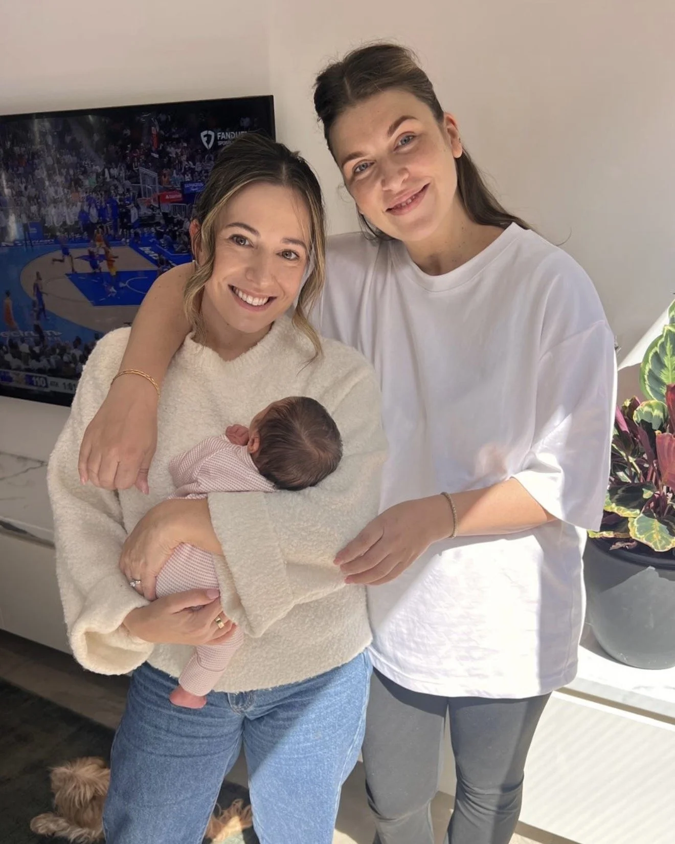 Steph the Doula standing with her client, Sharnelle Vella, holding her newborn baby in her Melbourne lounge room. Both are smiling while baby sleeps peacefully in Steph's arms.