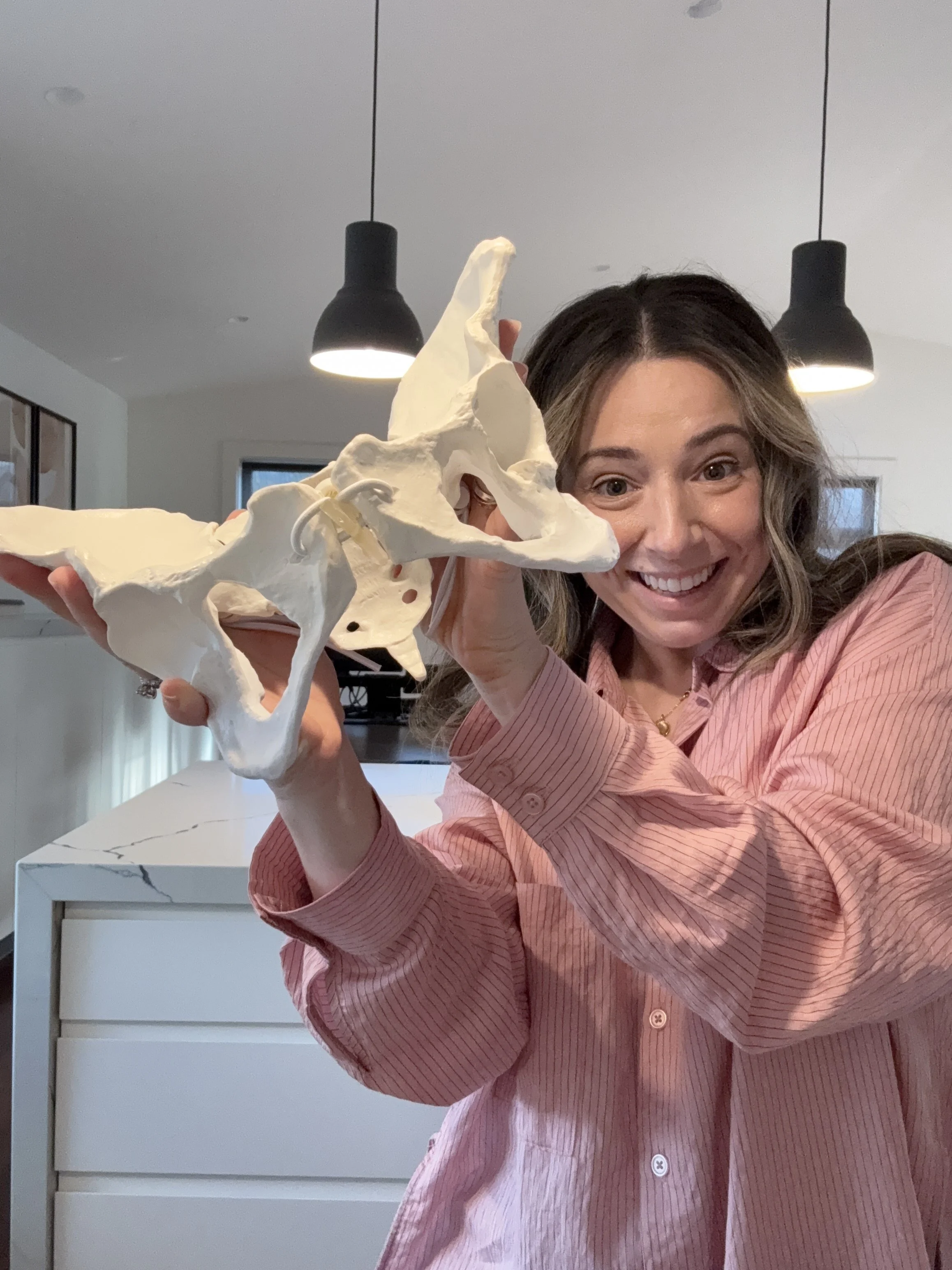 Steph the Doula in playfully showing a skeleton model of a human pelvis, with a smiling expression.