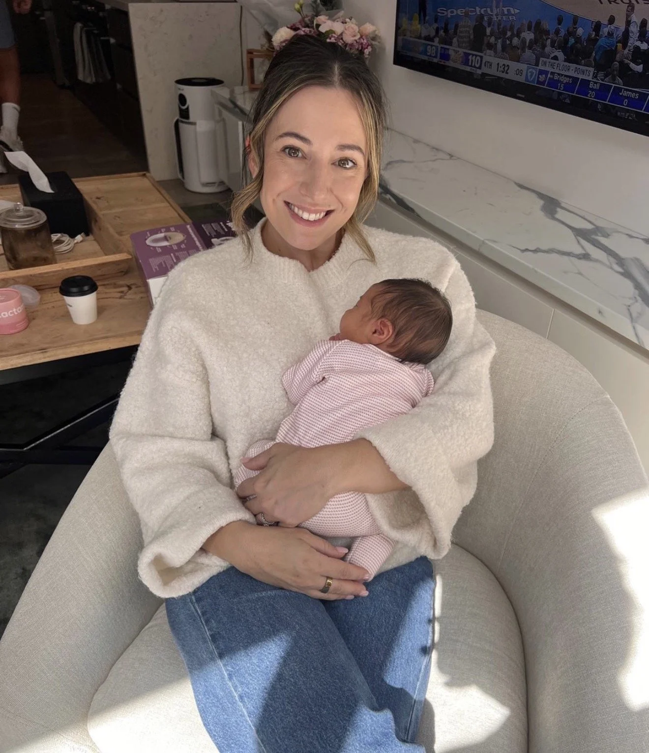 Steph Tsalacopoulos, Melbourne-based doula and founder of Steph the Doula. Holding a newborn, sitting in a cosy cream armchair.