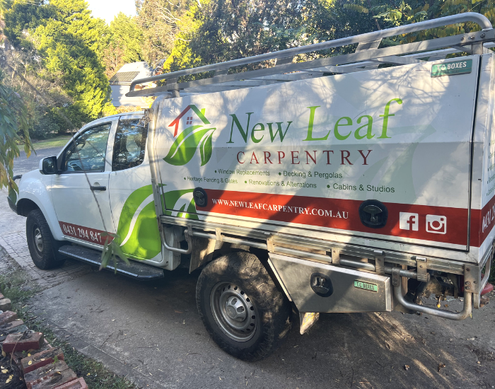 New Leaf Carpentry utility vehicle. The sign lists services like window replacements, decking, pergolas, fencing, renovations, and cabins, with contact information and website.