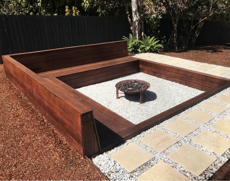 New Leaf Carpentry installation of modern outdoor backyard fire pit area with a square wooden fire pit, a gravel surround, and a paved walkway.