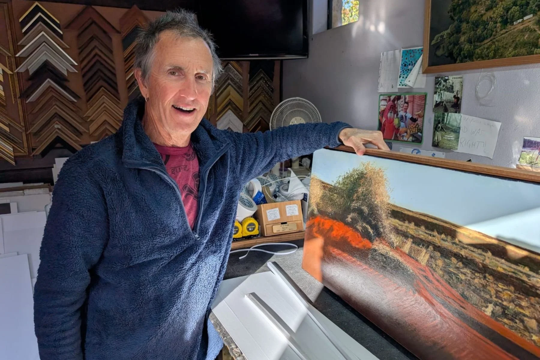 Cameron Coutts holding a custom float-framed canvas in his East Fremantle picture framing studio.