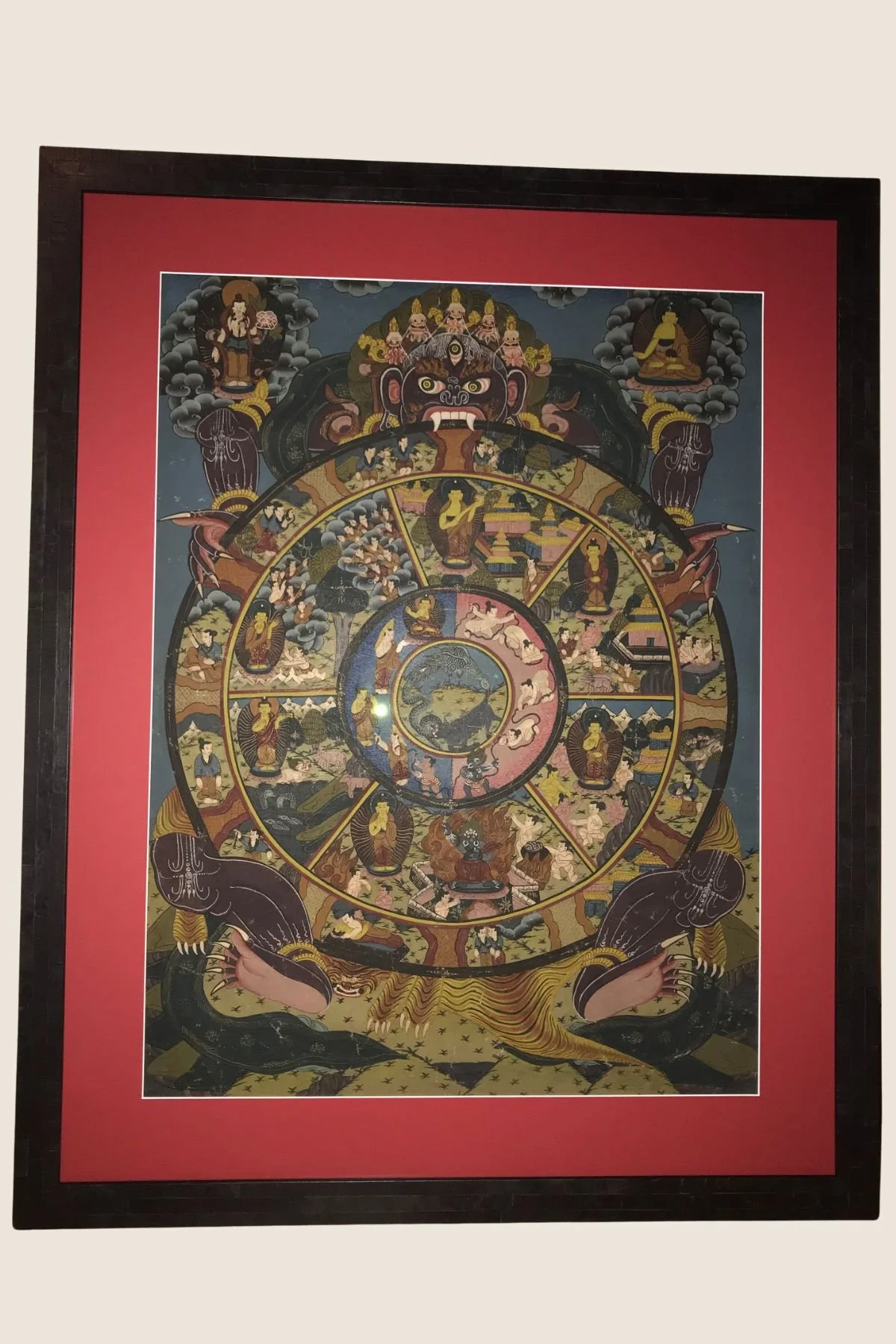 Tibetan Wheel of Life thangka in a dark wood frame, red mat
