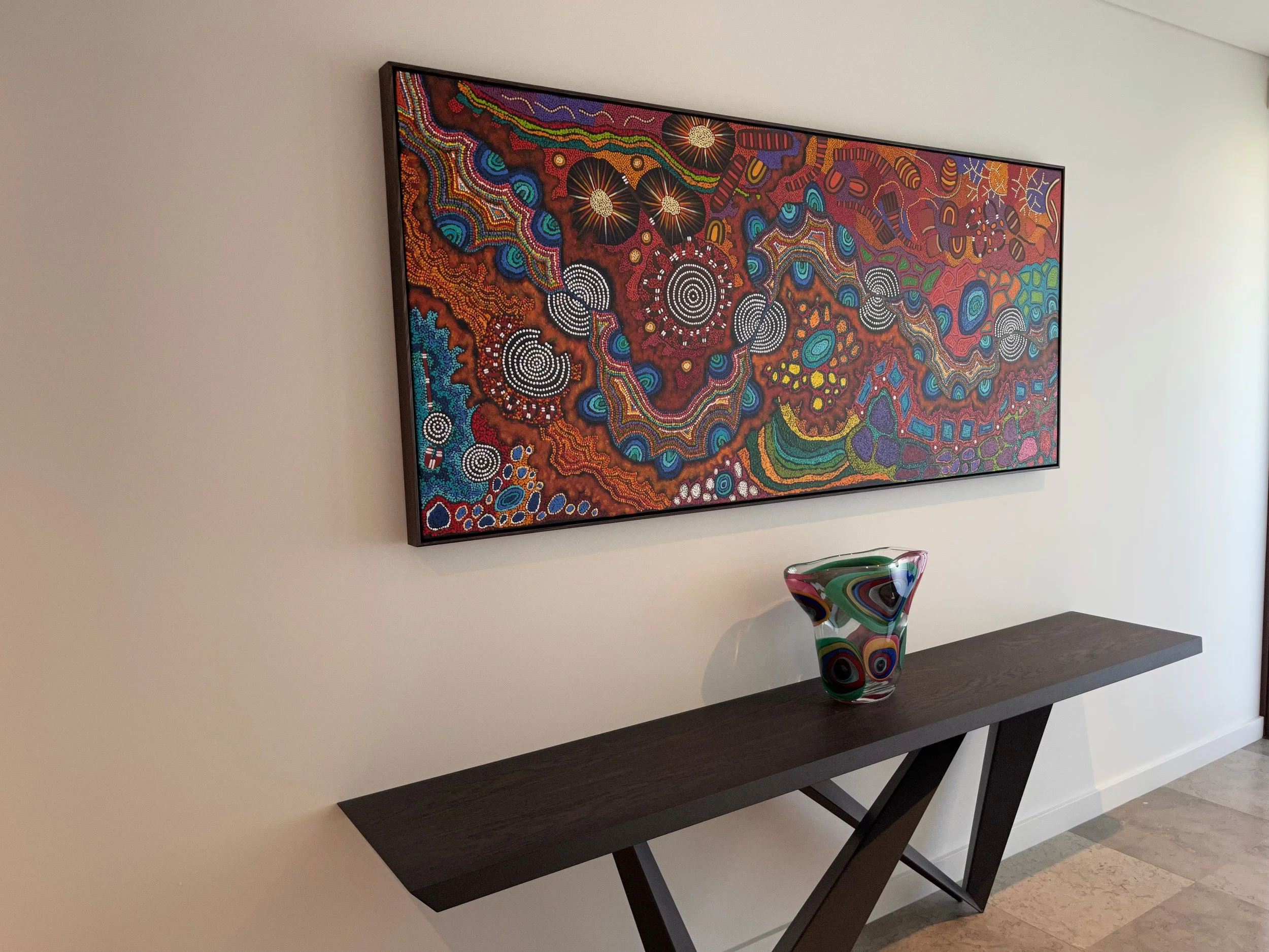 Aboriginal dot painting in a dark float frame, installed above console