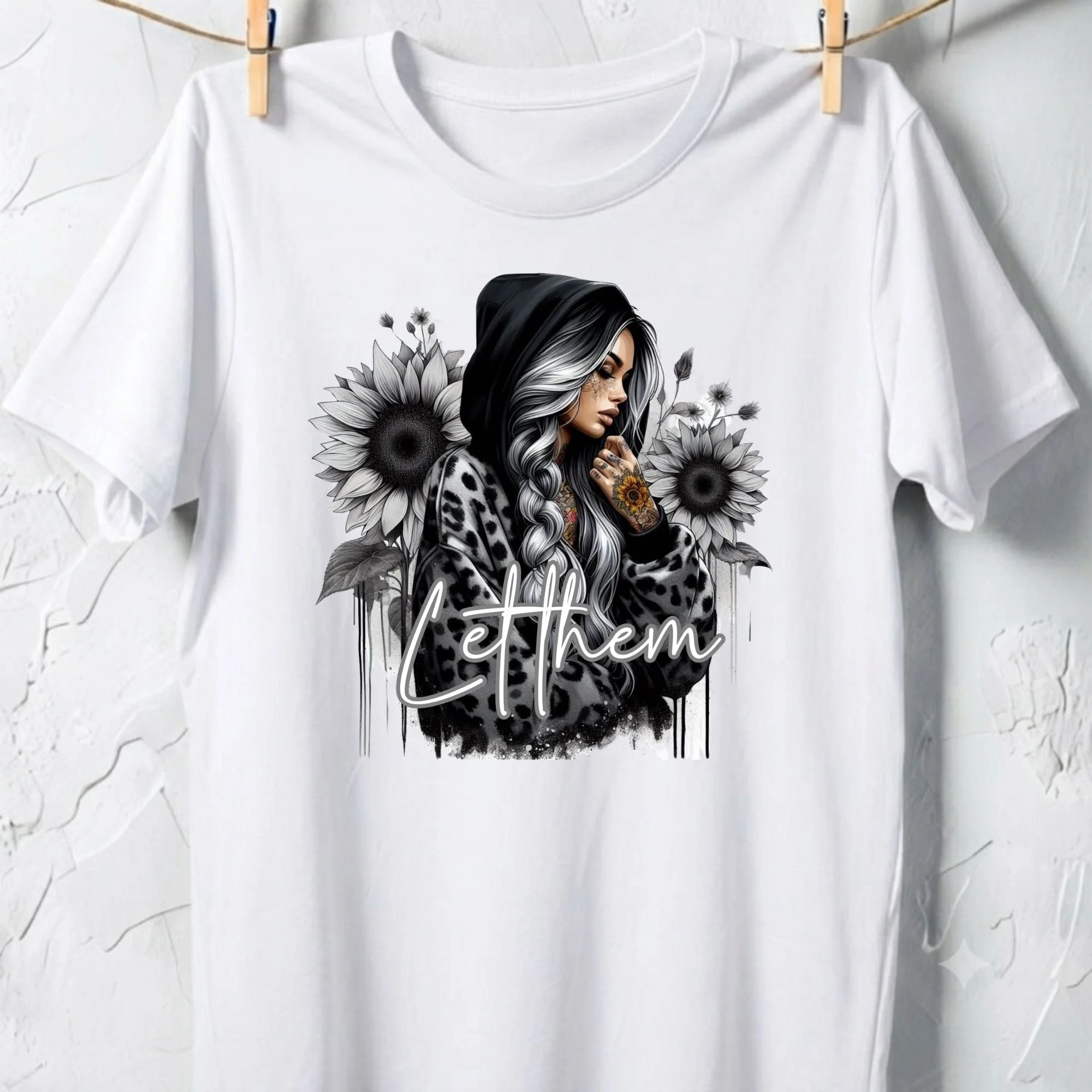 A white T-shirt hanging on a line with clothespins. The T-shirt has a black and white illustration of a woman with long hair, flowers, and the words 'Keep the' written on the bottom.