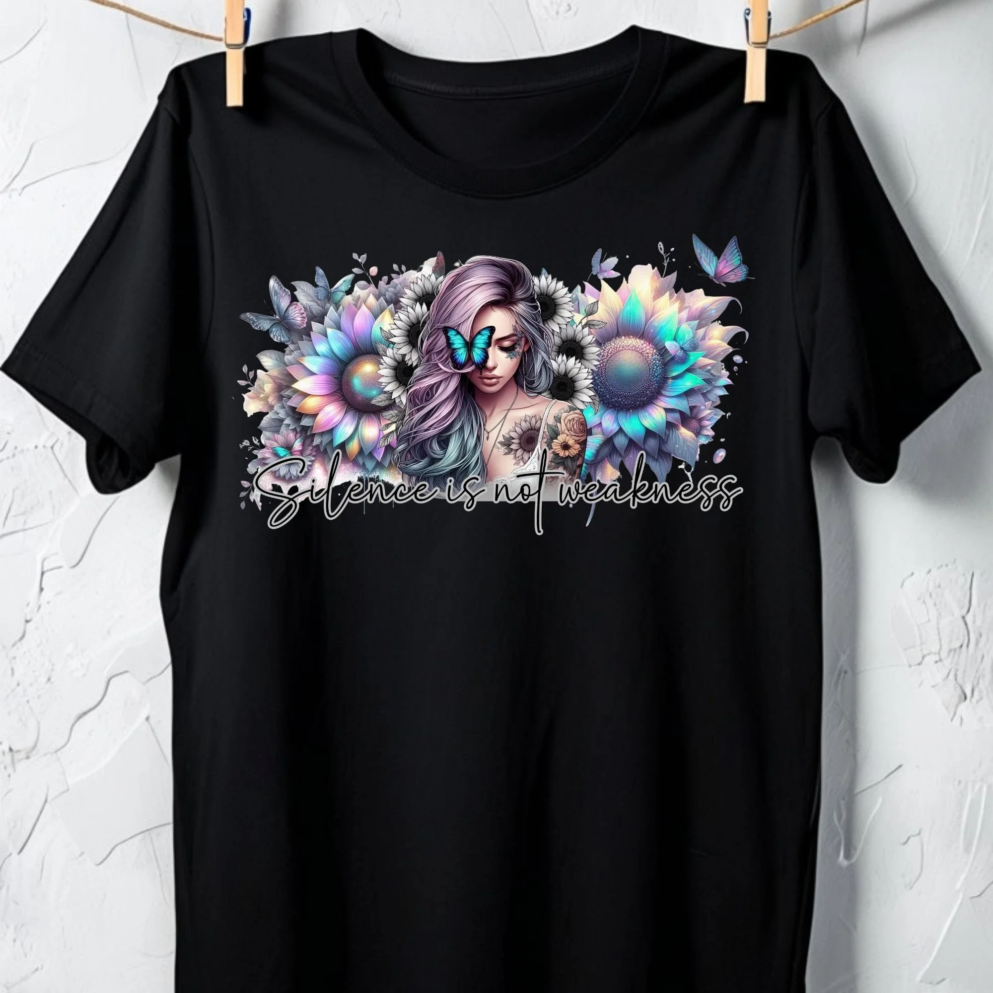 Black T-shirt with a colorful, fantasy-style illustration of a woman with long, purple hair, surrounded by sunflowers and butterflies, and the phrase "Silence is not weakness" written at the bottom.