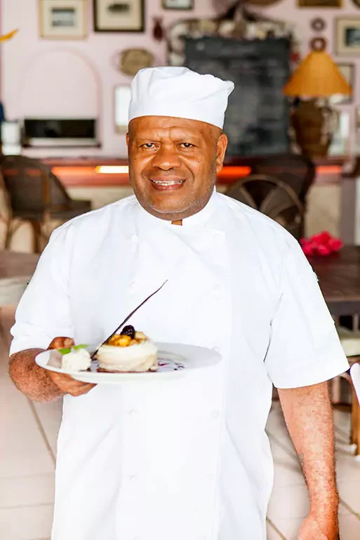 Chef in white uniform and hat holding a plate with a dessert in a restaurant.