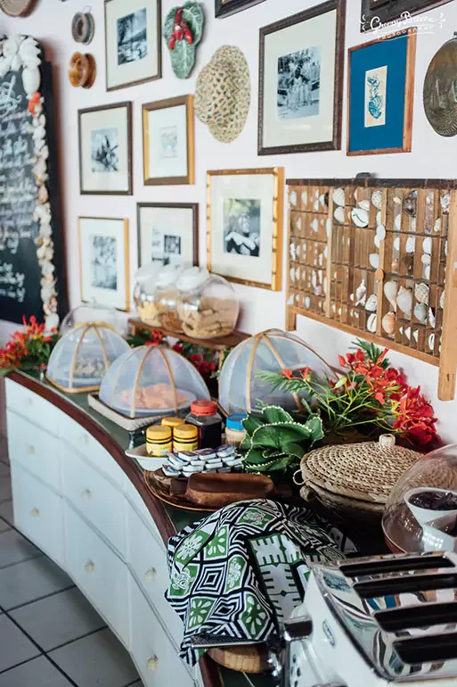 A decorated holiday-themed kitchen or dining area with assorted jars, covered dishes, and festive decorations, including poinsettias and greenery, on a white curved cabinet. The wall features a gallery of framed pictures, wreath, and wooden decorativ