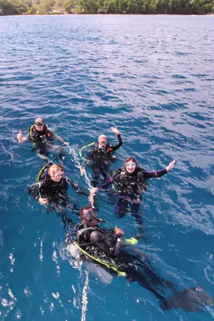 Five people in wetsuits swimming and floating in the ocean near the shoreline.
