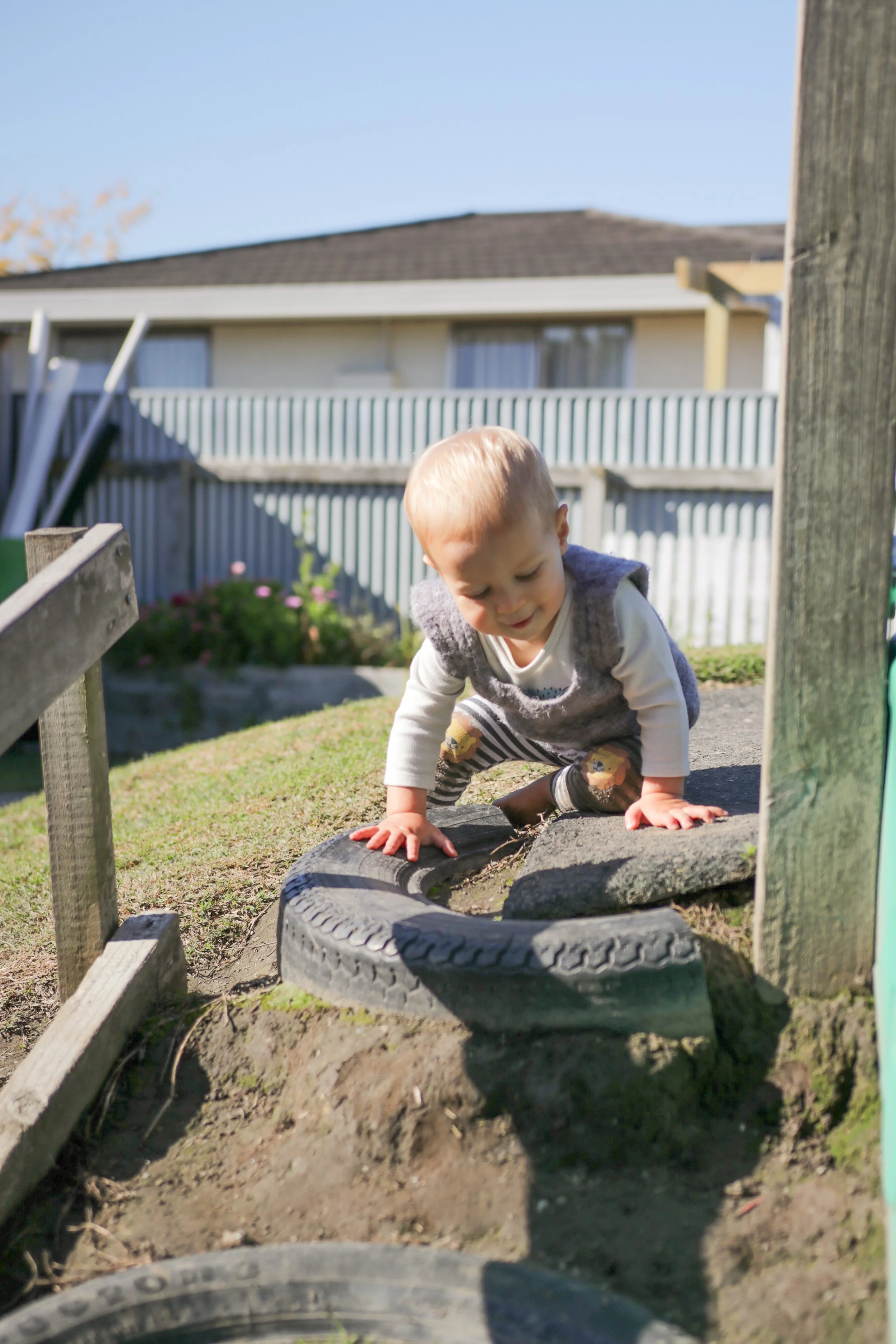 A young child crawling over a small obstacle course made of tires outside in a backyard.