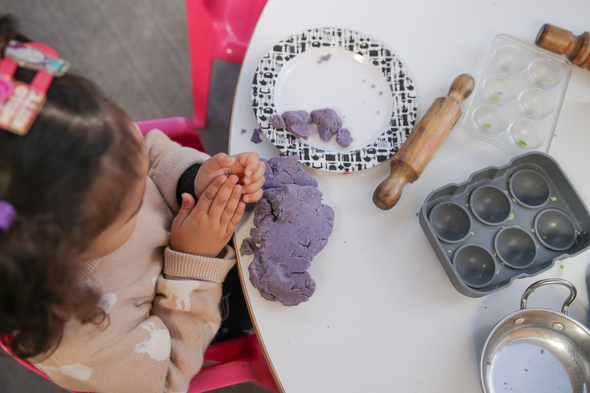 Children making purple dough or clay at a craft or cooking station.
