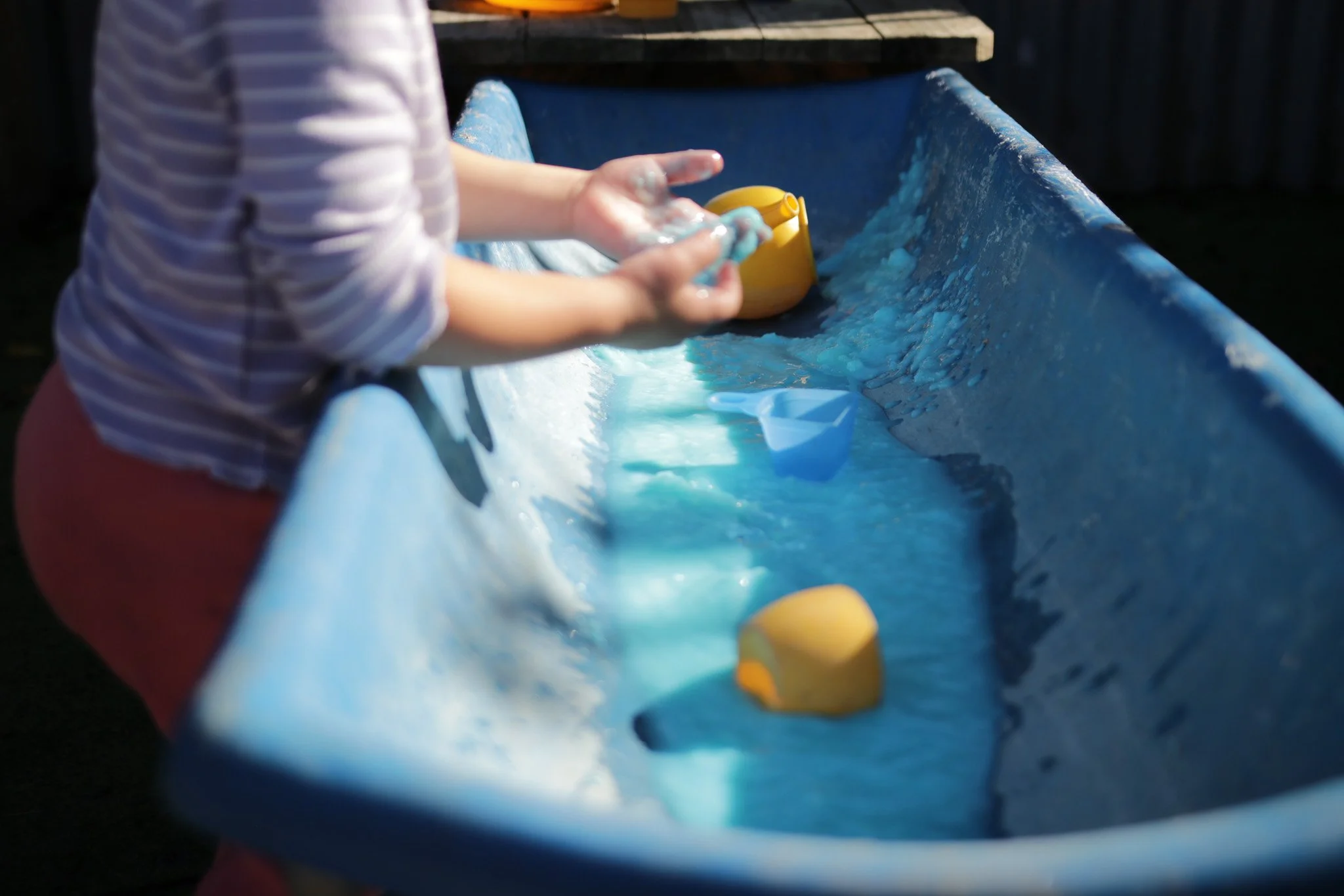 Child playing with water in a blue slip and slide, holding a yellow toy.