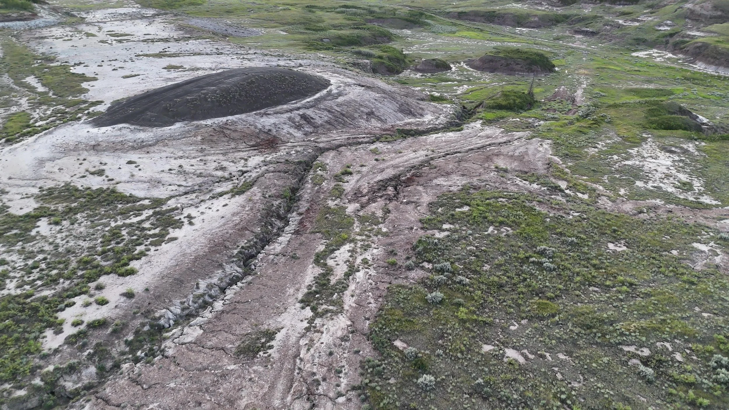 A barren, rugged landscape with sparse vegetation, erosion channels, and damaged landscape from sodium bentonite clay mine that was abandoned 50 years ago, but the landscape has not recovered.