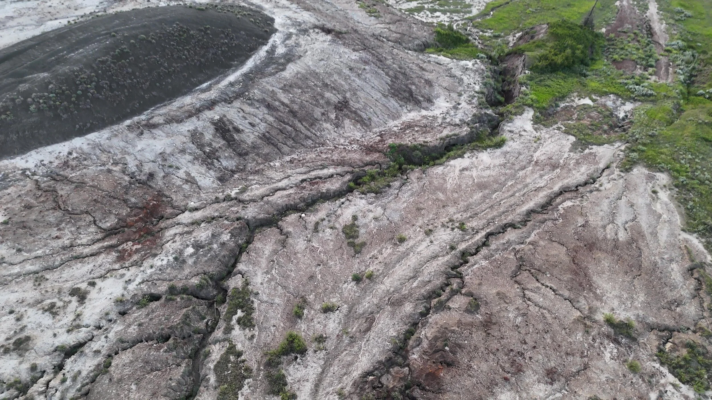 Aerial view of eroded sandy terrain with layered rock formations and sparse green vegetation, a mining scar from sodium bentonite clay mining at the Dressler mine from 50 year ago.
