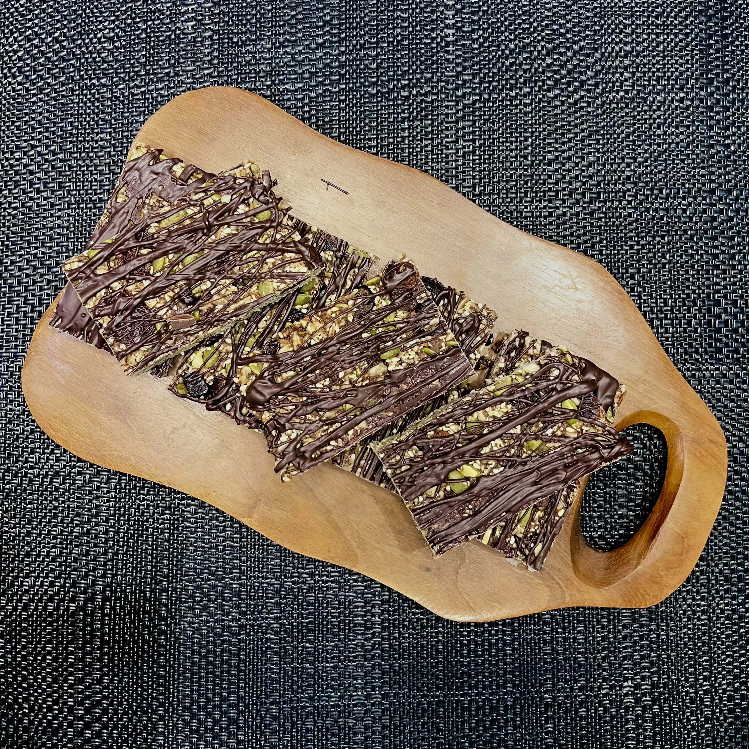 Sliced dessert bar with a chocolate drizzle topping and crushed nuts on a wooden cutting board.