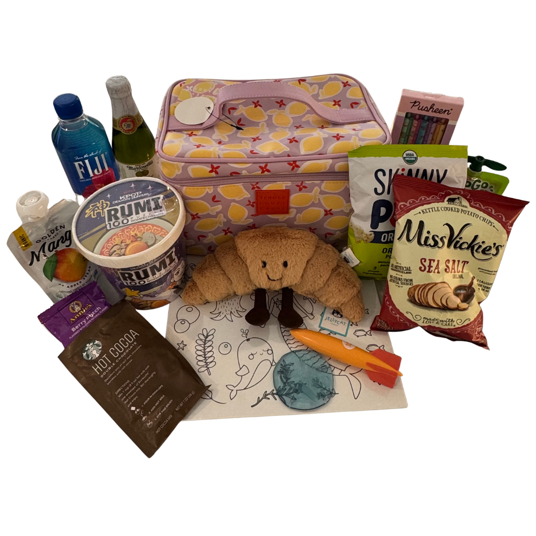 A collection of travel and snack items including a pink and floral patterned Kids Keepsake bag, including a Jellycat stuffie, Fiji water, mini cider, KPop Demon Hunters puzzle, kettle chips, hot cocoa packet, and coloring sheet with crayons.