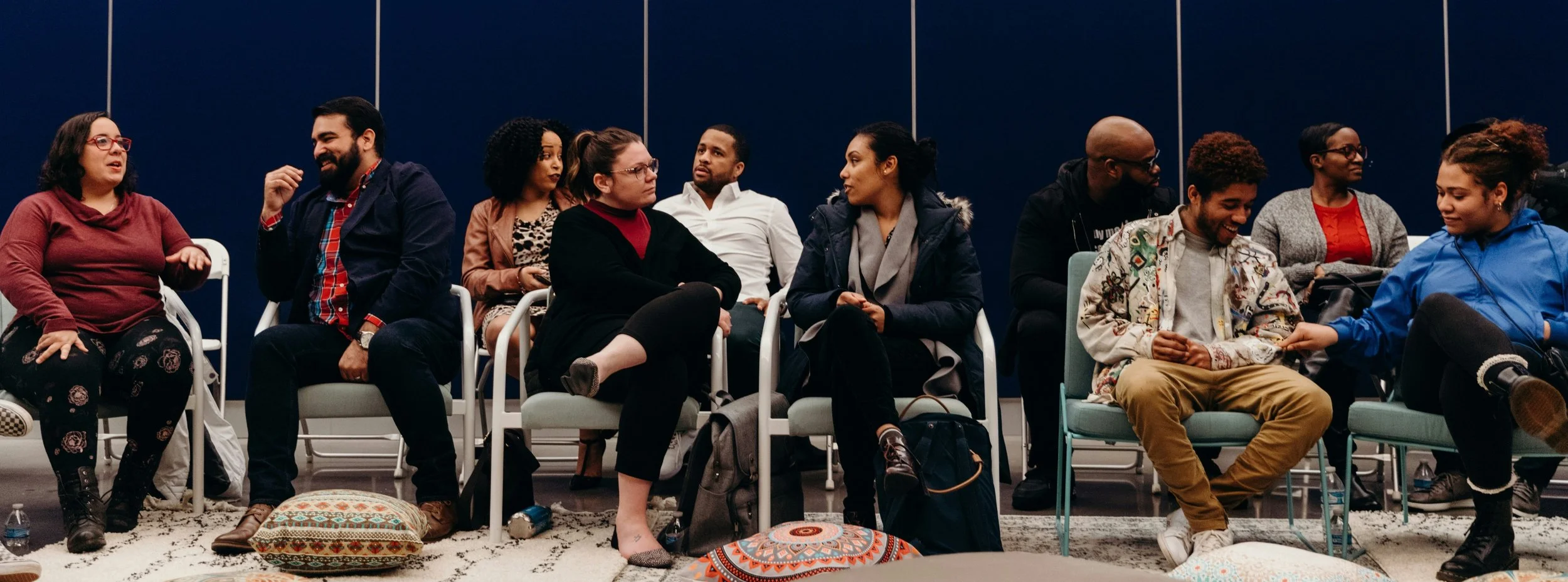 group of 10-12 racially diverse people sigging in chairs side by side, speaking in each other in pairs