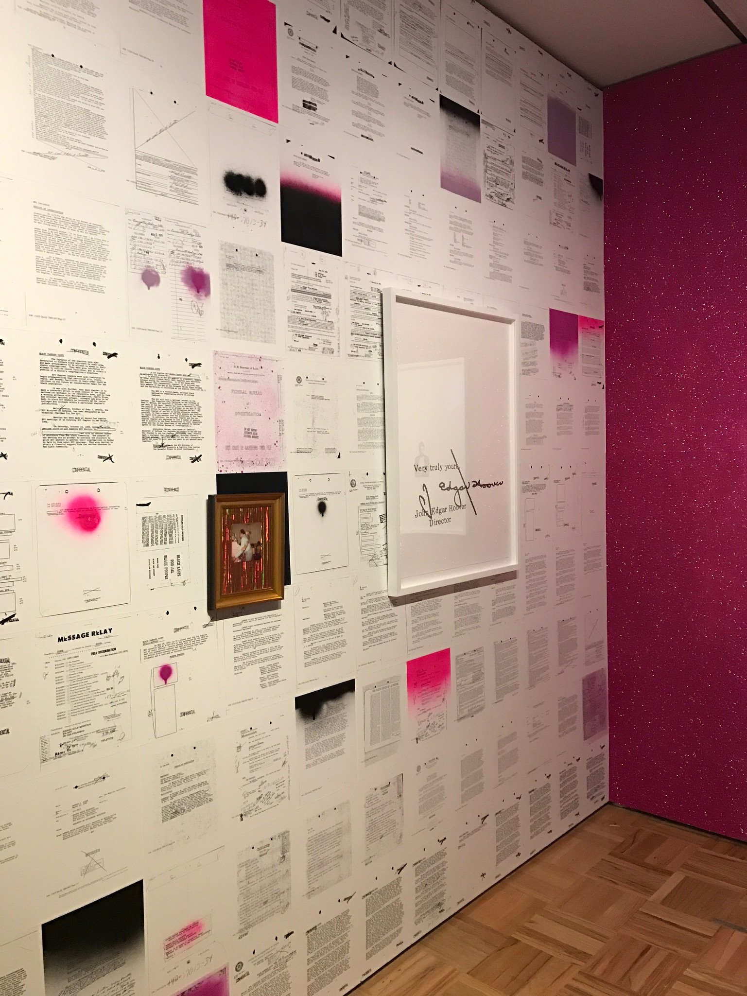 Documents plastered on the wall at an art exhibit. In the center is a framed document with the words "Very truly yours, J Edgar Hoover"