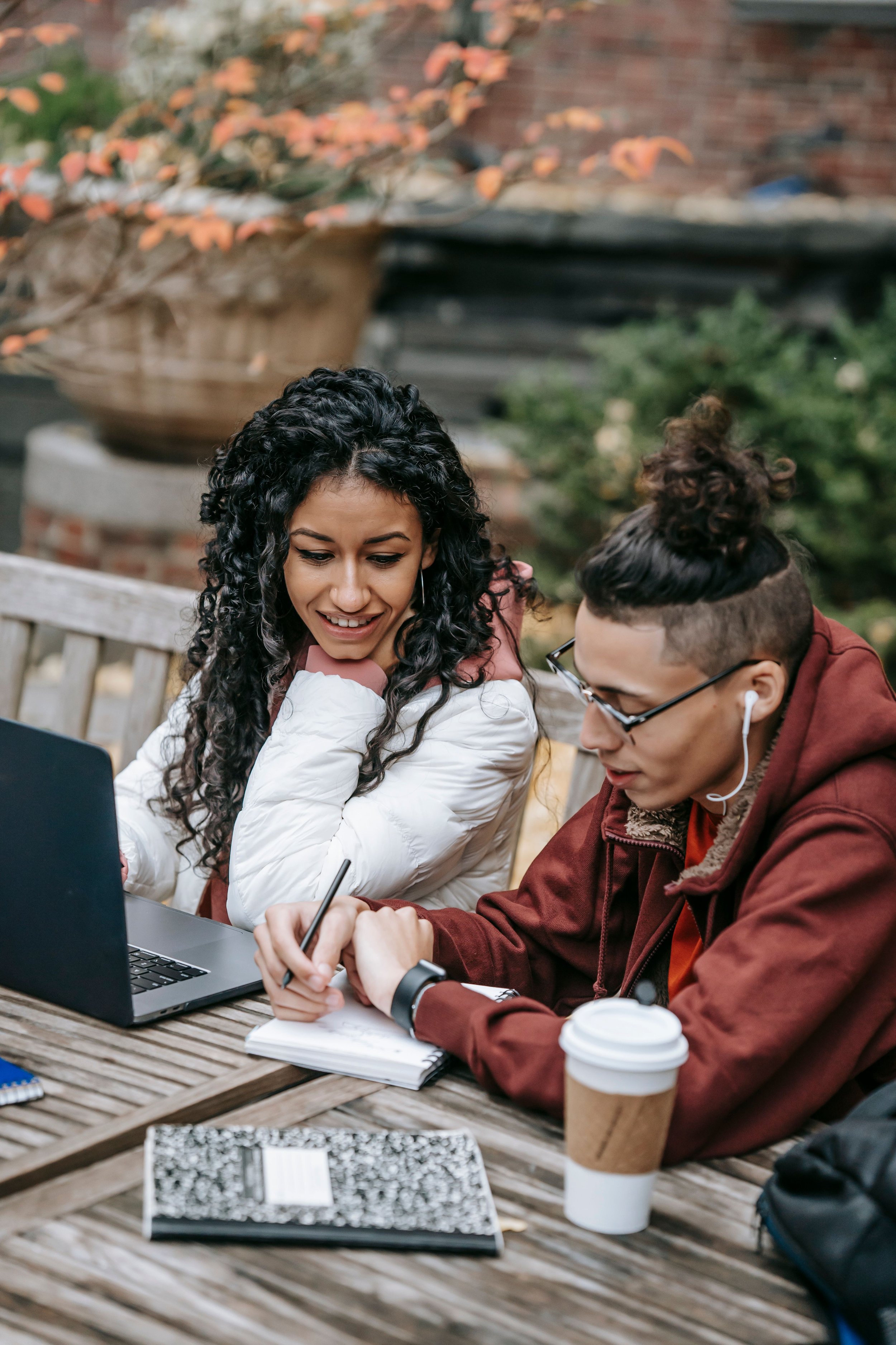 two adults sitting side by side in front of a computer and looking at a notepad