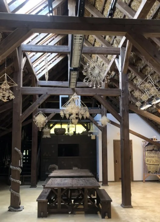 Dark wood beams and tables under a wooden roof with various woven mobiles hanging from the roof
