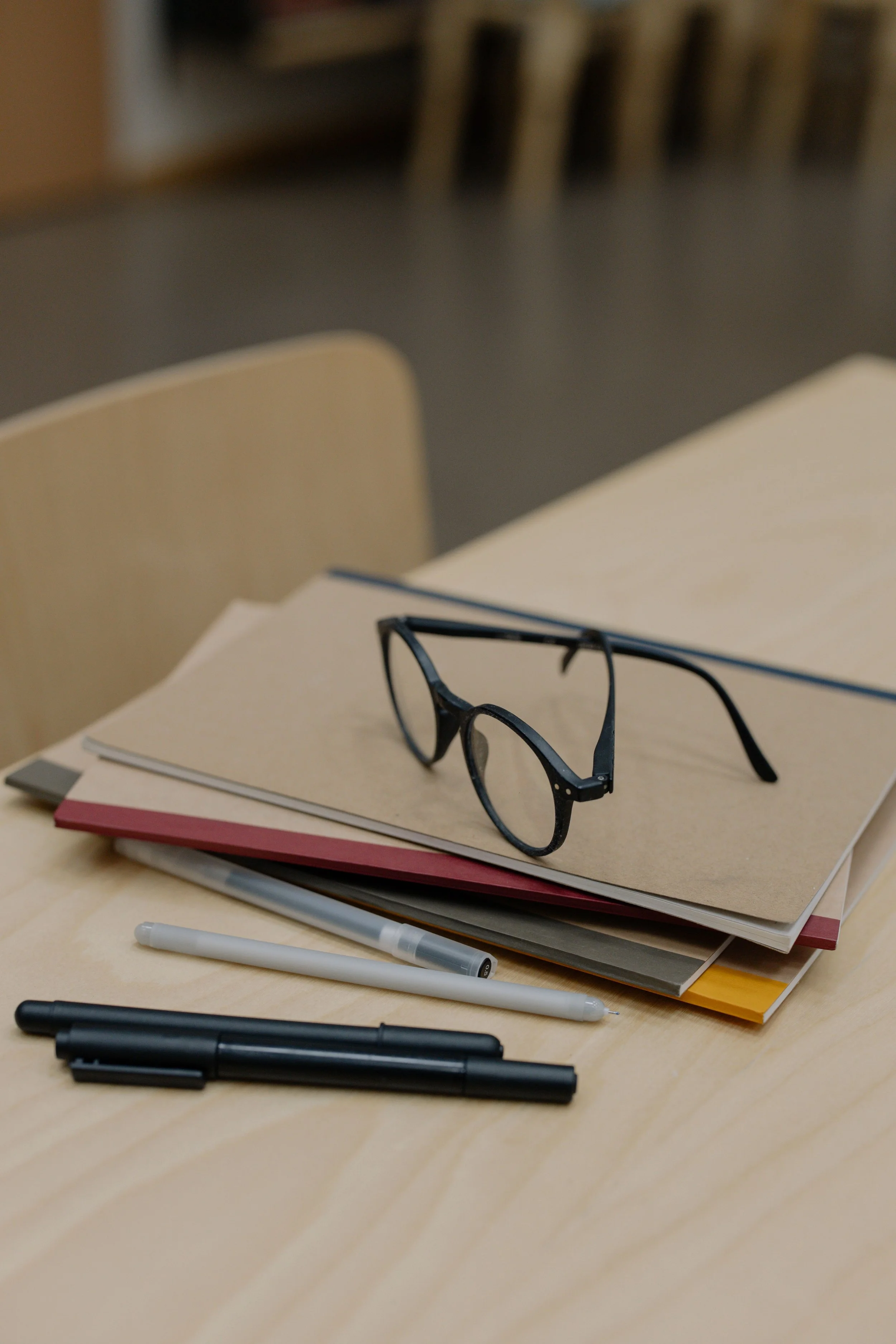 pair of glasses on a pile of notebooks and pens