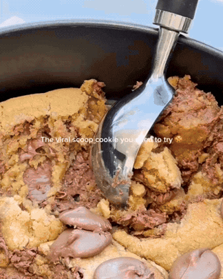 Chocolate chip cookie dough being scooped from a mixing bowl with an ice cream scoop.