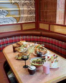 A restaurant booth with a marble table set with various dishes, including salads, drinks, and small plates, in a cozy decorated space.