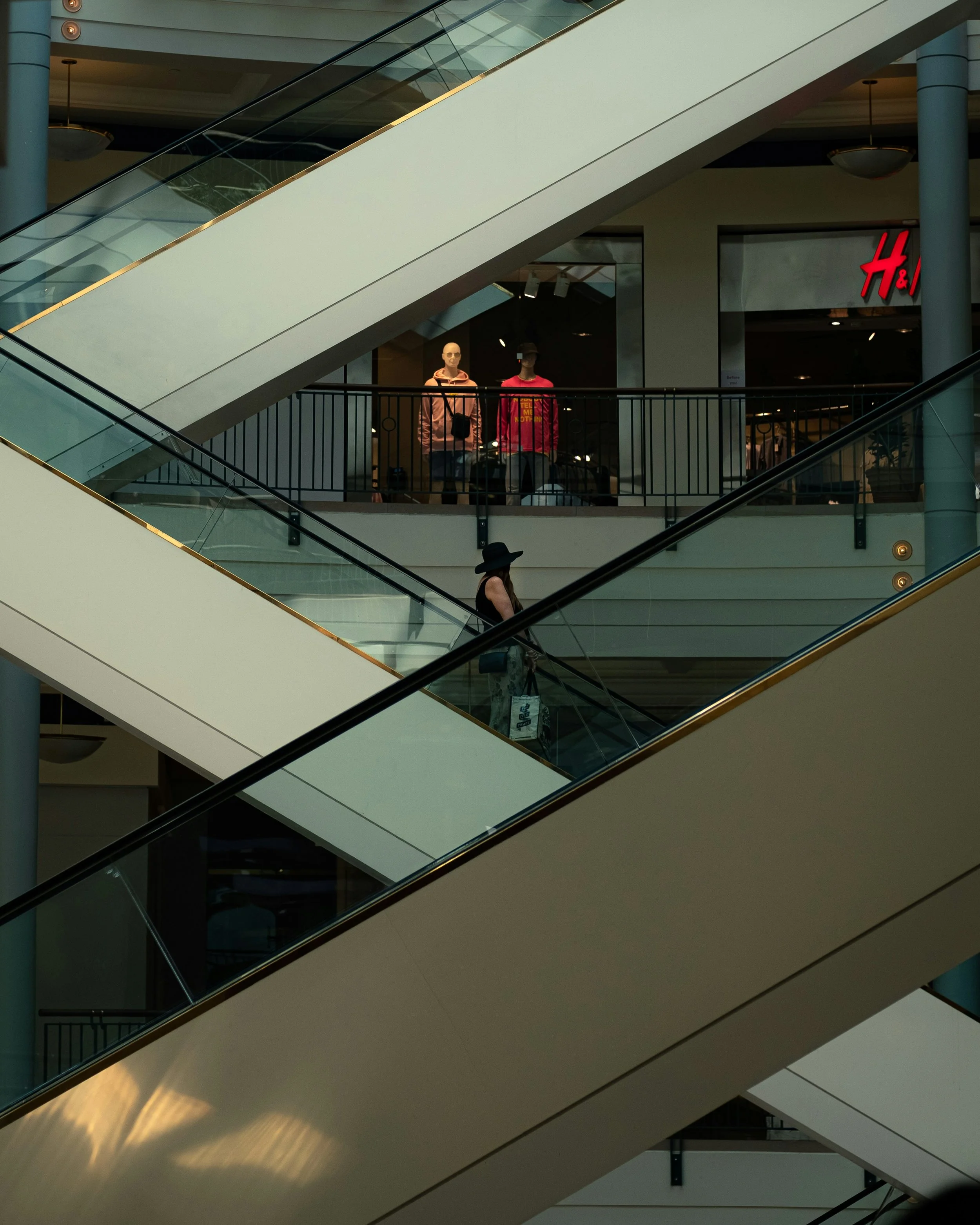 Multiple escalators in a shopping mall, with mannequins dressed in clothing behind glass on the upper level.